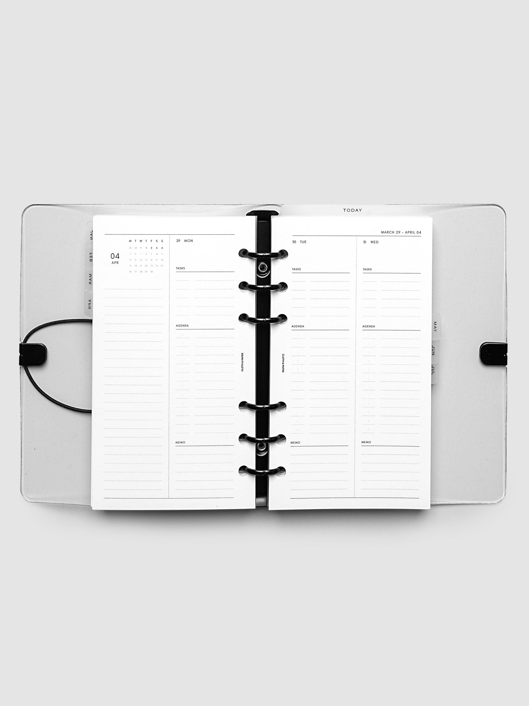 Flat lay of an open planner with black 6-ring binding at the center, a Monday through Wednesday spread across two facing pages with a mini monthly calendar, daily tasks, agenda, and memo sections, Personal 6-Ring Punch size