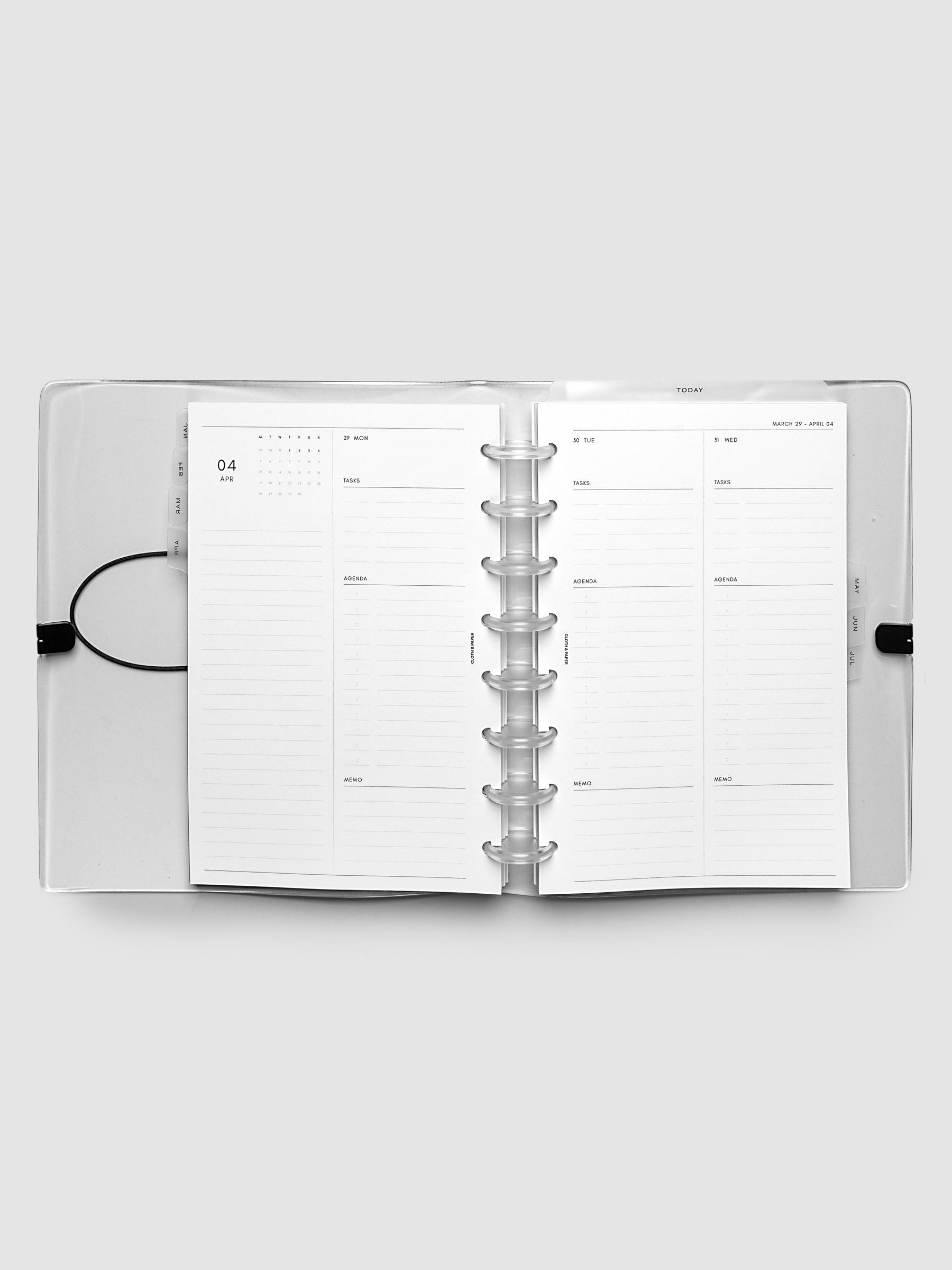 Flat lay of an open planner with clear 8-disc binding at the center, a Monday through Wednesday spread across two facing pages with a mini monthly calendar, daily tasks, agenda, and memo sections, Half Letter 8-Disc Punch size