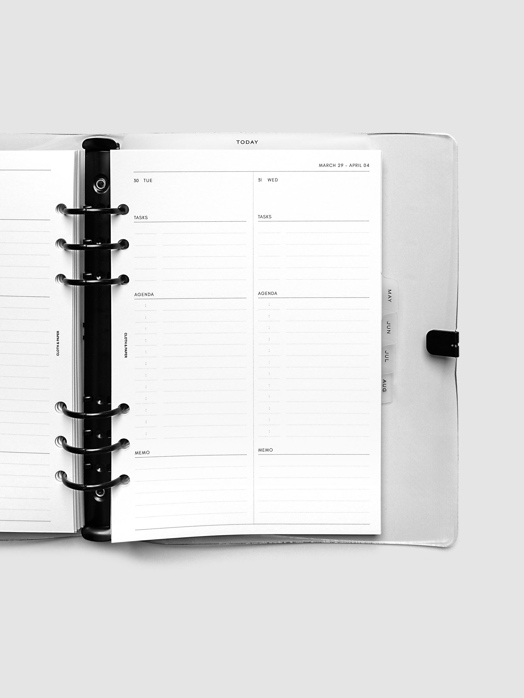 Open planner with black 6-ring binding, weekly spread on the right page showing Tuesday and Wednesday daily columns with tasks, agenda, and memo sections, tabbed monthly dividers visible at the edge, A5 6-Ring Punch size