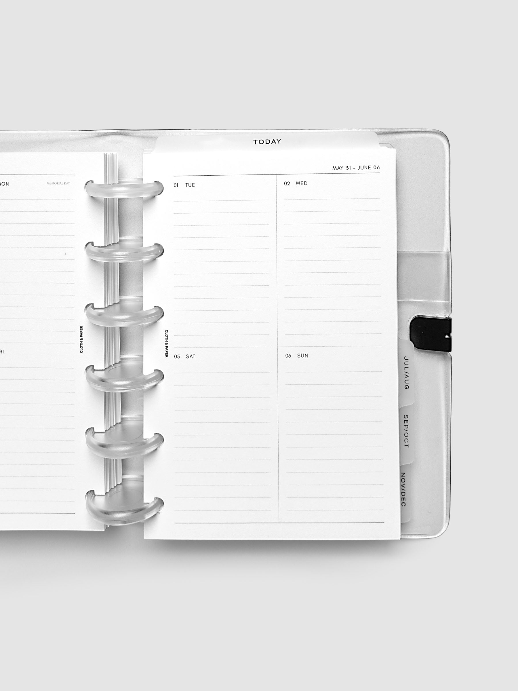 Close-up of an open planner with clear 6-disc binding, weekly vertical spread showing Tuesday through Sunday in a two-column grid with lined daily sections, tabbed monthly dividers visible at the edge, CP Petite 6-Disc Punch size
