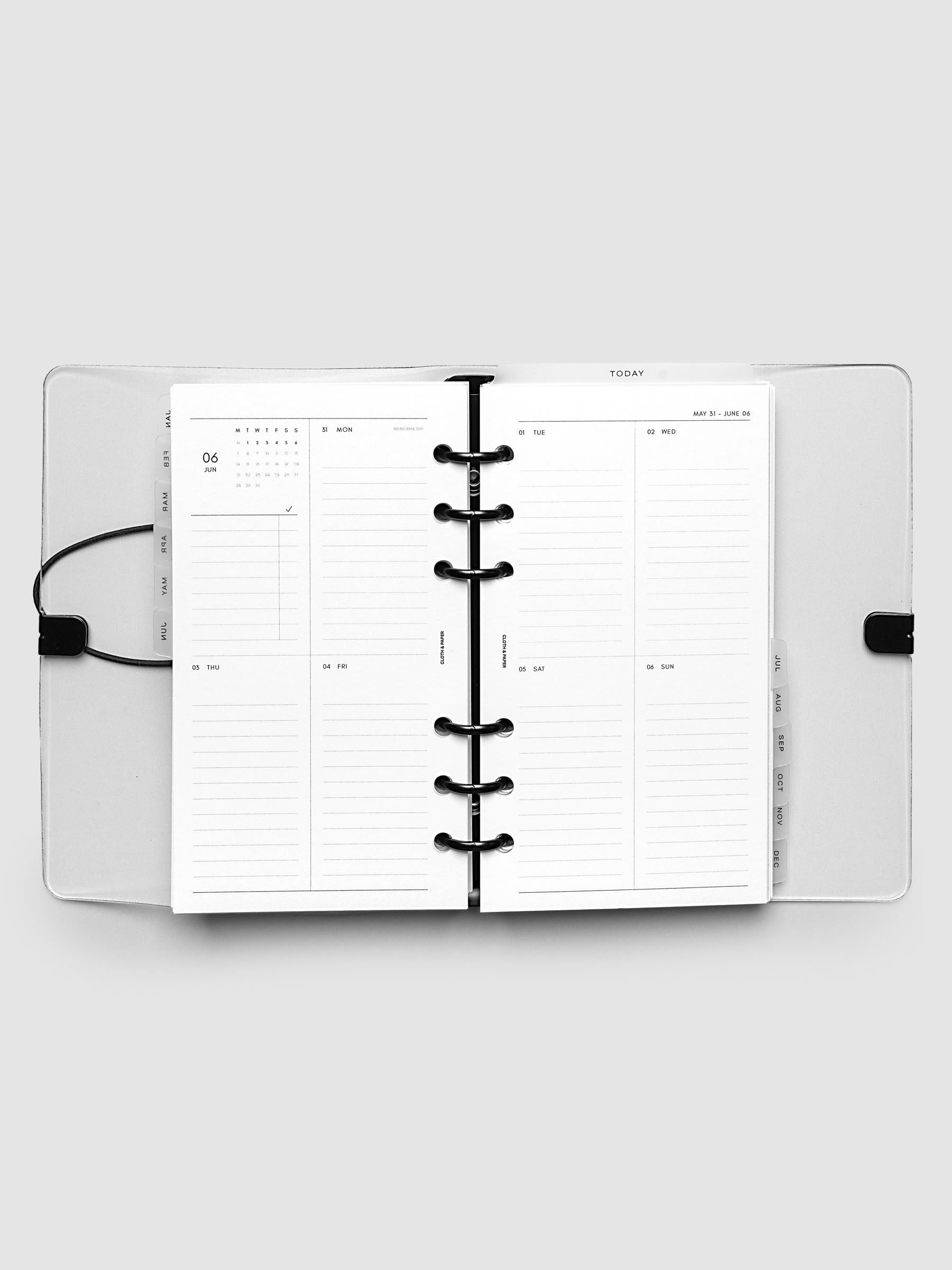 Flat lay of an open planner with black 6-ring binding at the center, a Monday through Sunday weekly vertical spread across two facing pages with a mini calendar and lined daily sections, Personal 6-Ring Punch size