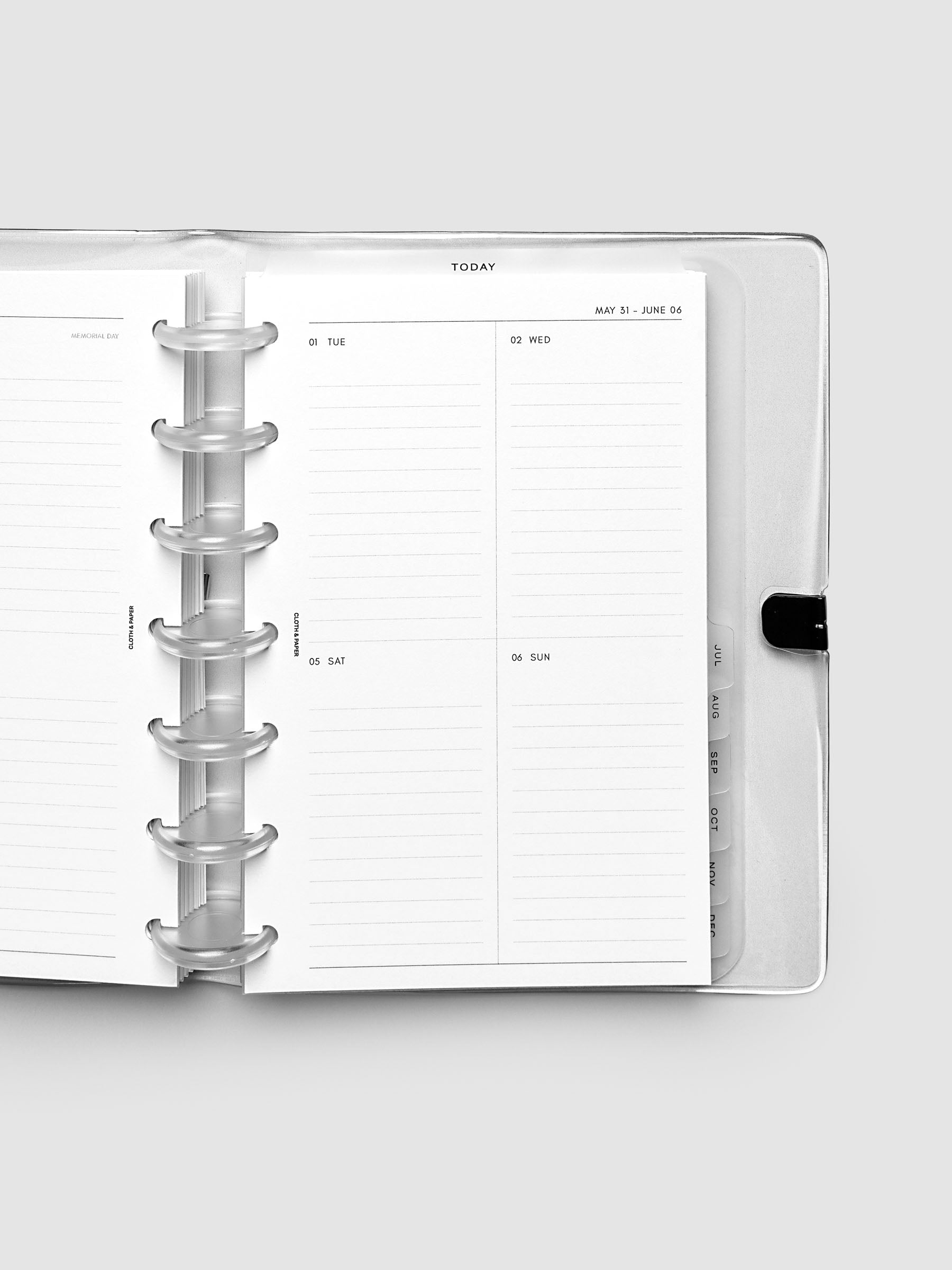 Close-up of an open planner with clear 7-disc binding, weekly vertical spread showing Tuesday through Sunday in a two-column grid with lined daily sections, tabbed monthly dividers visible at the edge, HP Mini 7-Disc Punch size