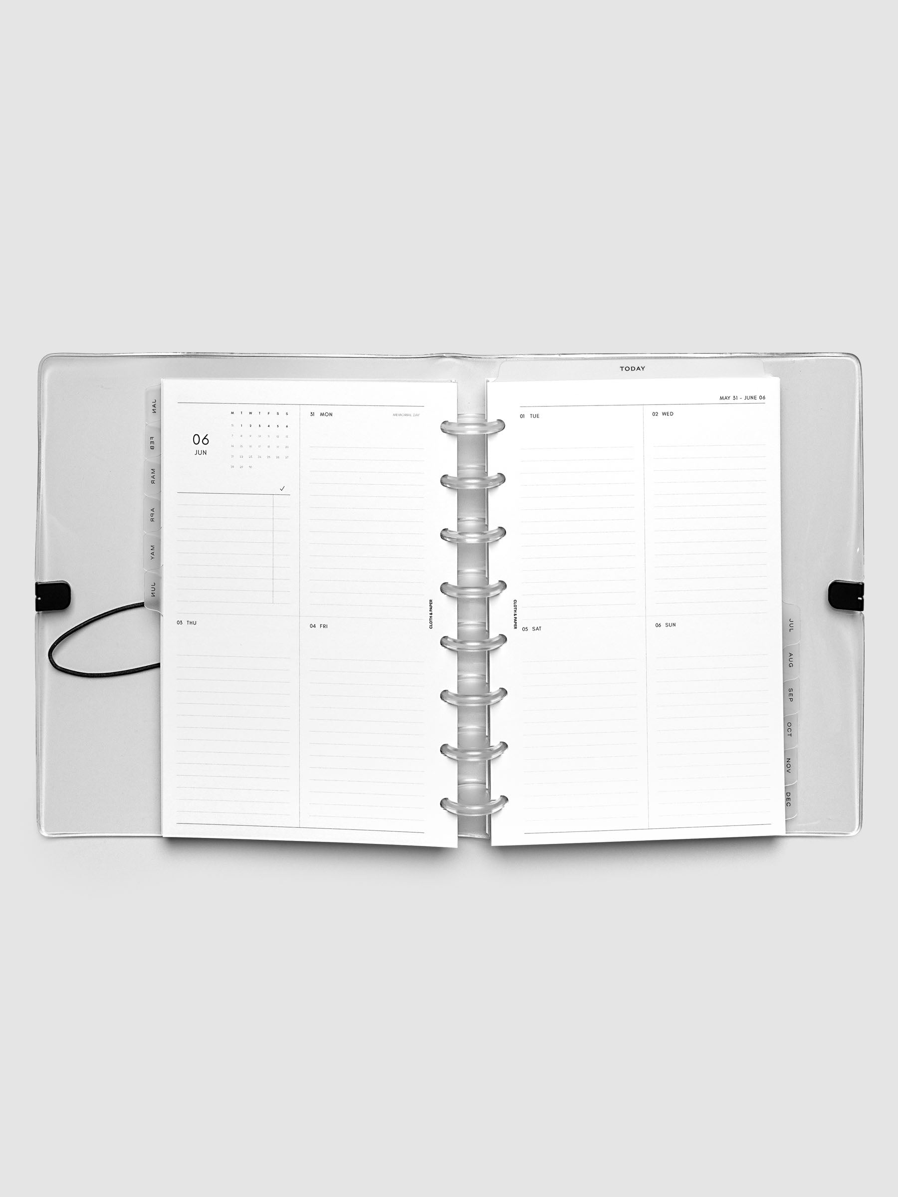 Flat lay of an open planner with clear 8-disc binding at the center, a Monday through Sunday weekly vertical spread across two facing pages with a mini calendar and lined daily sections, Half Letter 8-Disc Punch size