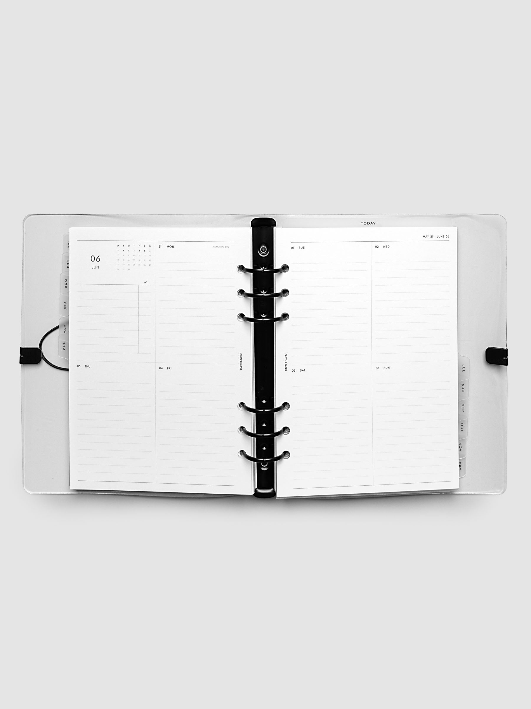 Flat lay of an open planner with black 6-ring binding at the center, a Monday through Sunday weekly vertical spread across two facing pages with a mini calendar and lined daily sections, A5 6-Ring Punch size