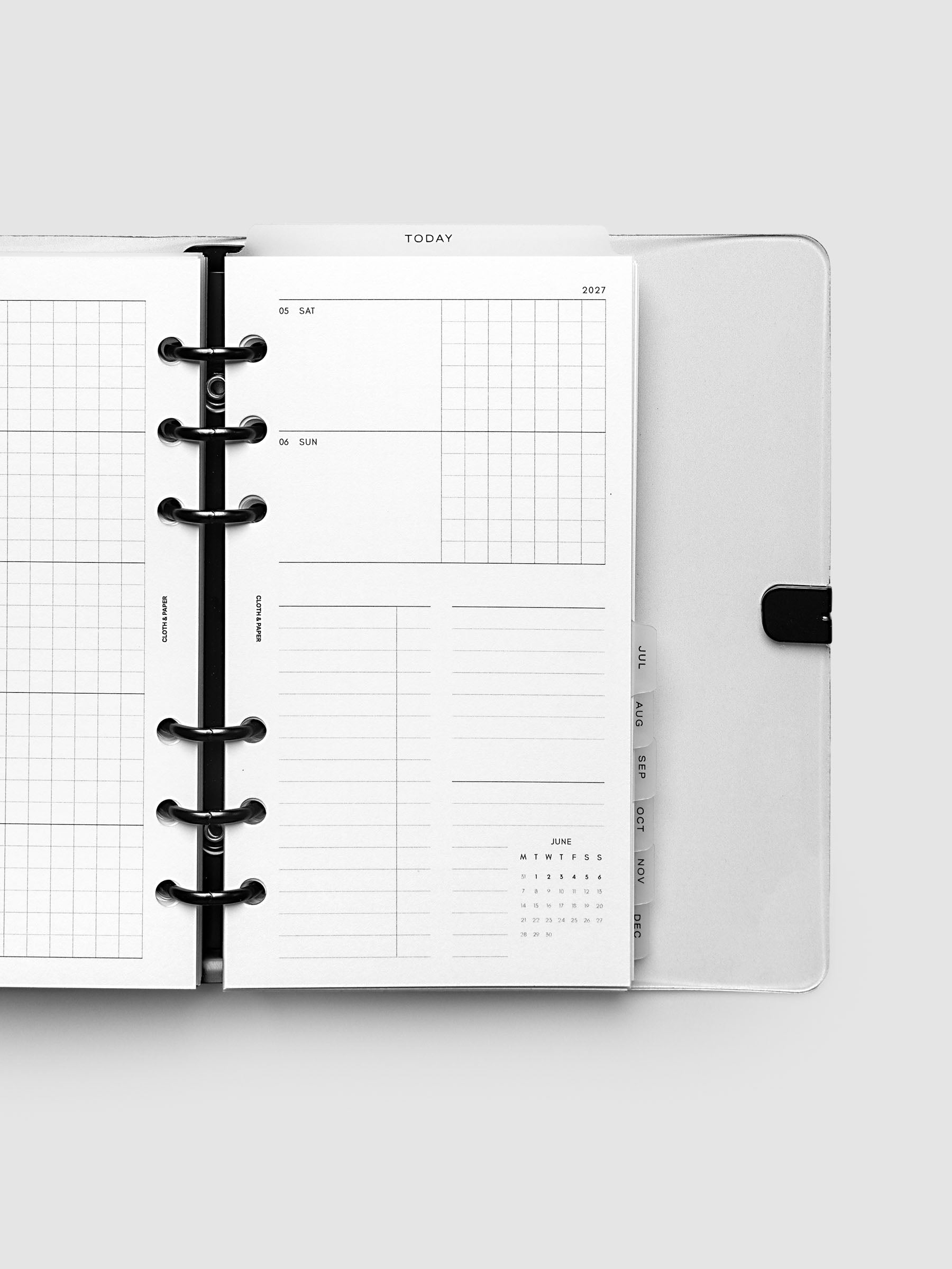 Close-up of an open planner with black 6-ring binding, weekly horizontal spread showing Saturday and Sunday in a shared row split into lined and graph columns, tabbed monthly dividers visible at the edge, Personal 6-Ring Punch size