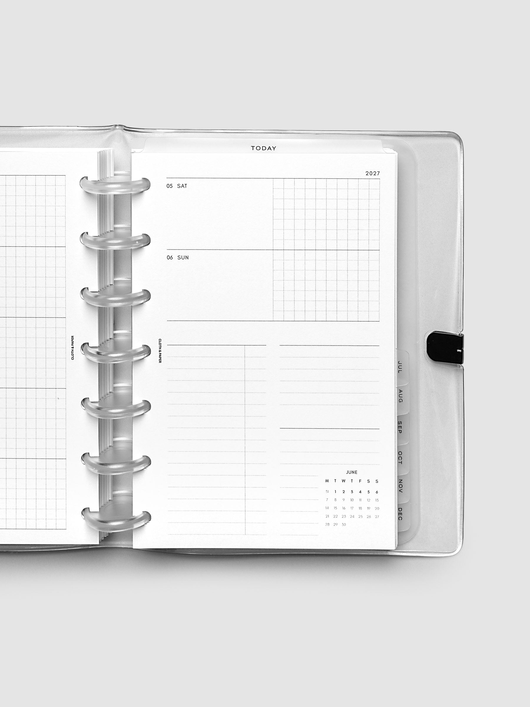 Close-up of an open planner with clear 7-disc binding, weekly horizontal spread showing Saturday and Sunday in a shared row split into lined and graph columns, tabbed monthly dividers visible at the edge, HP Mini 7-Disc Punch size
