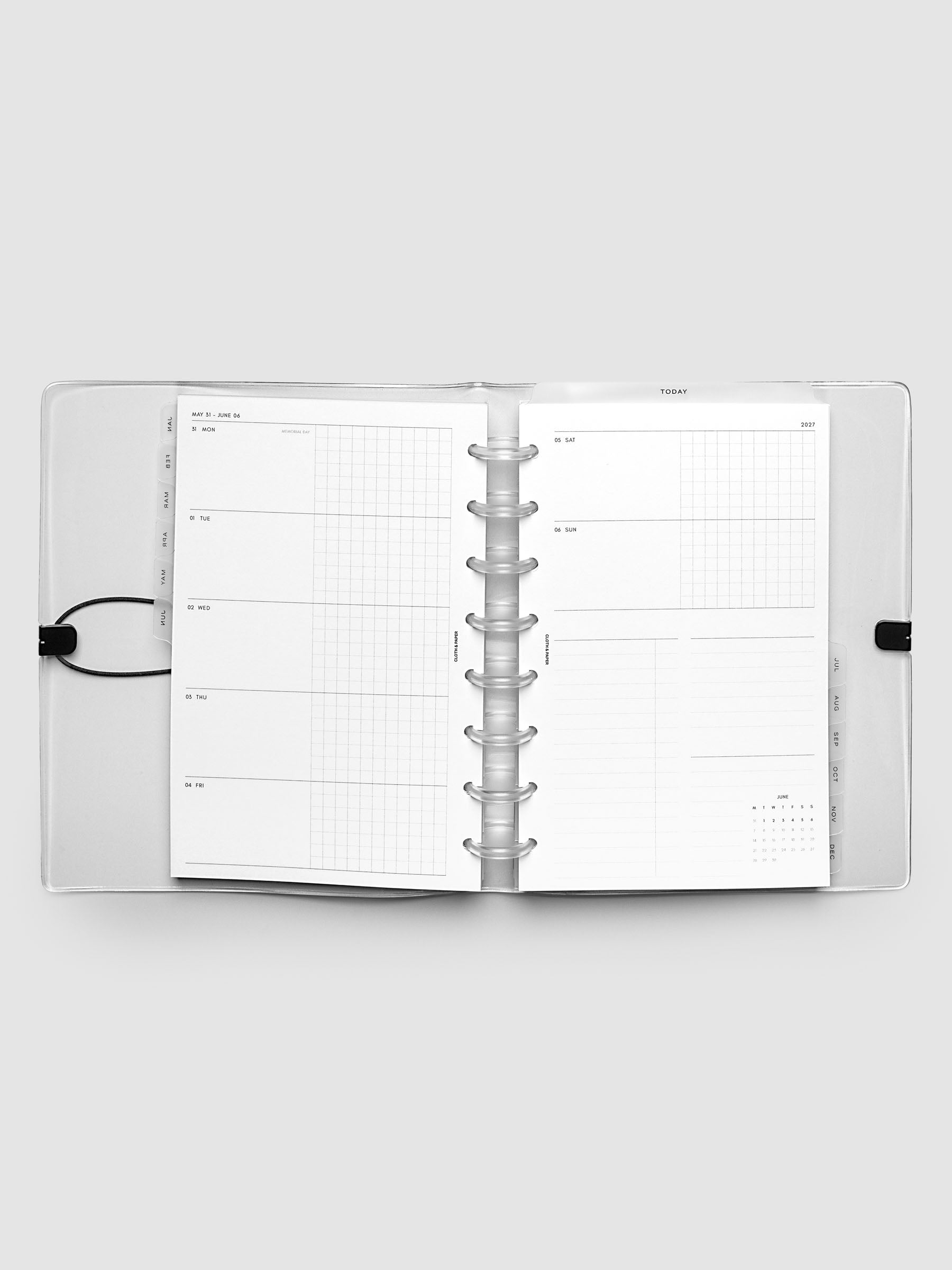 Flat lay of an open planner with clear 8-disc binding at the center, a Monday through Sunday weekly horizontal spread across two facing pages with a tasks and notes section and mini calendar, Half Letter 8-Disc Punch size