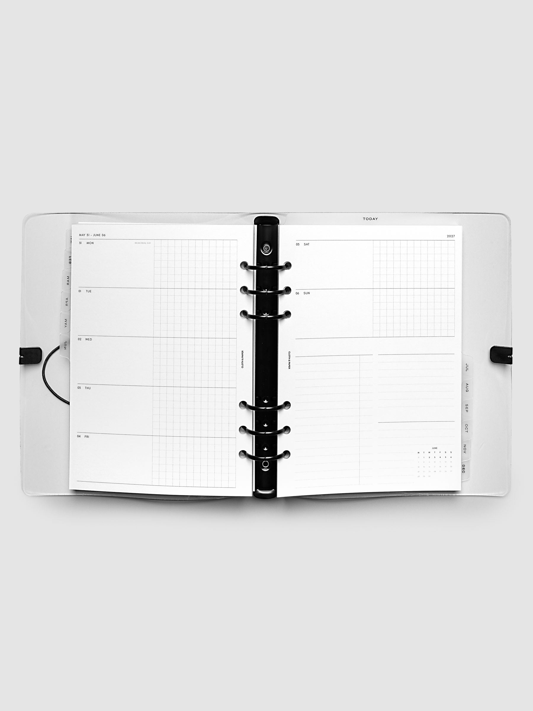 Flat lay of an open planner with black 6-ring binding at the center, a Monday through Sunday weekly horizontal spread across two facing pages with a tasks and notes section and mini calendar, A5 6-Ring Punch size