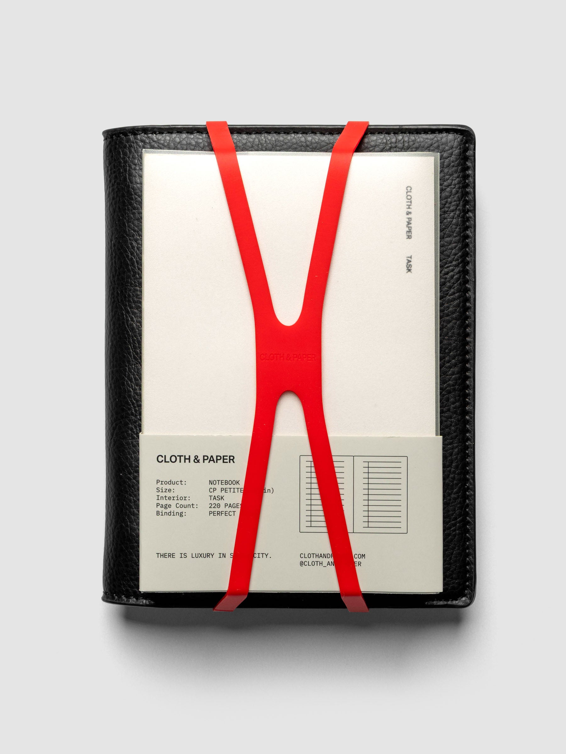 Small, red planner closure band shown holding a CP Petite perfect bound notebook on a CP Petite leather planner cover.