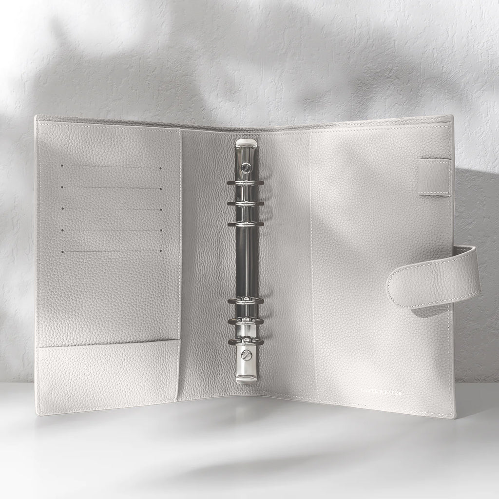 Ash  leather agenda displayed on an off-white background. It is opened to display the silver hardware and company foil stamp.