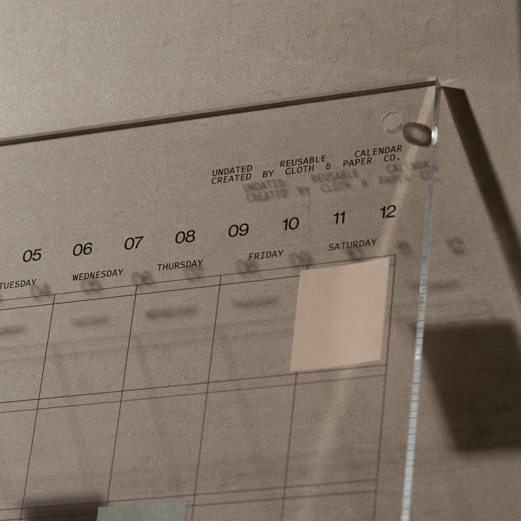 Close up of calendar on a warmly lit background. A sticky note has been placed over the "Saturday" box and fits perfectly within the square.