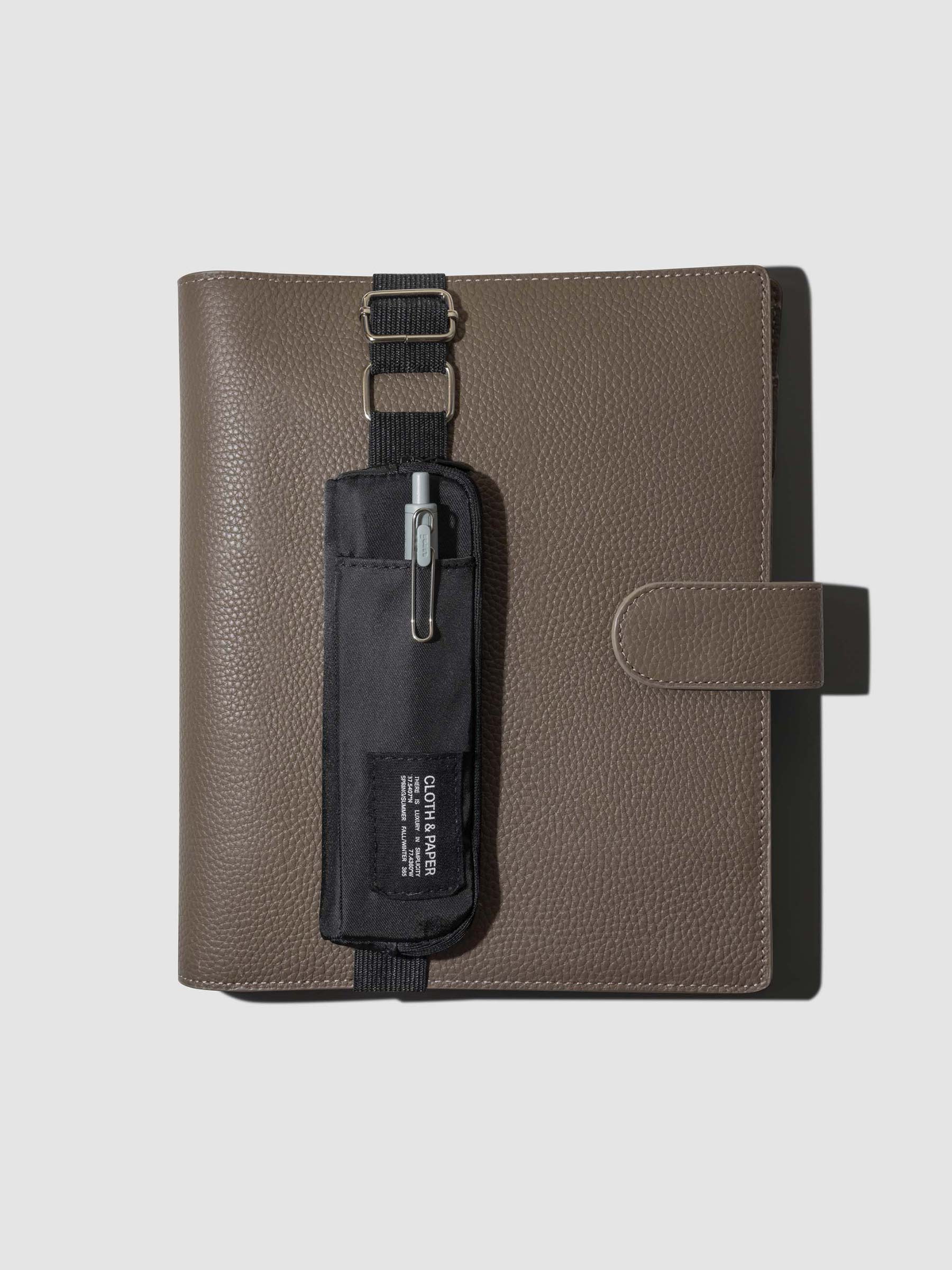 Notebook pouch displayed strapped to a brown leather folio on a neutral background. Color shown is Avant Garde.