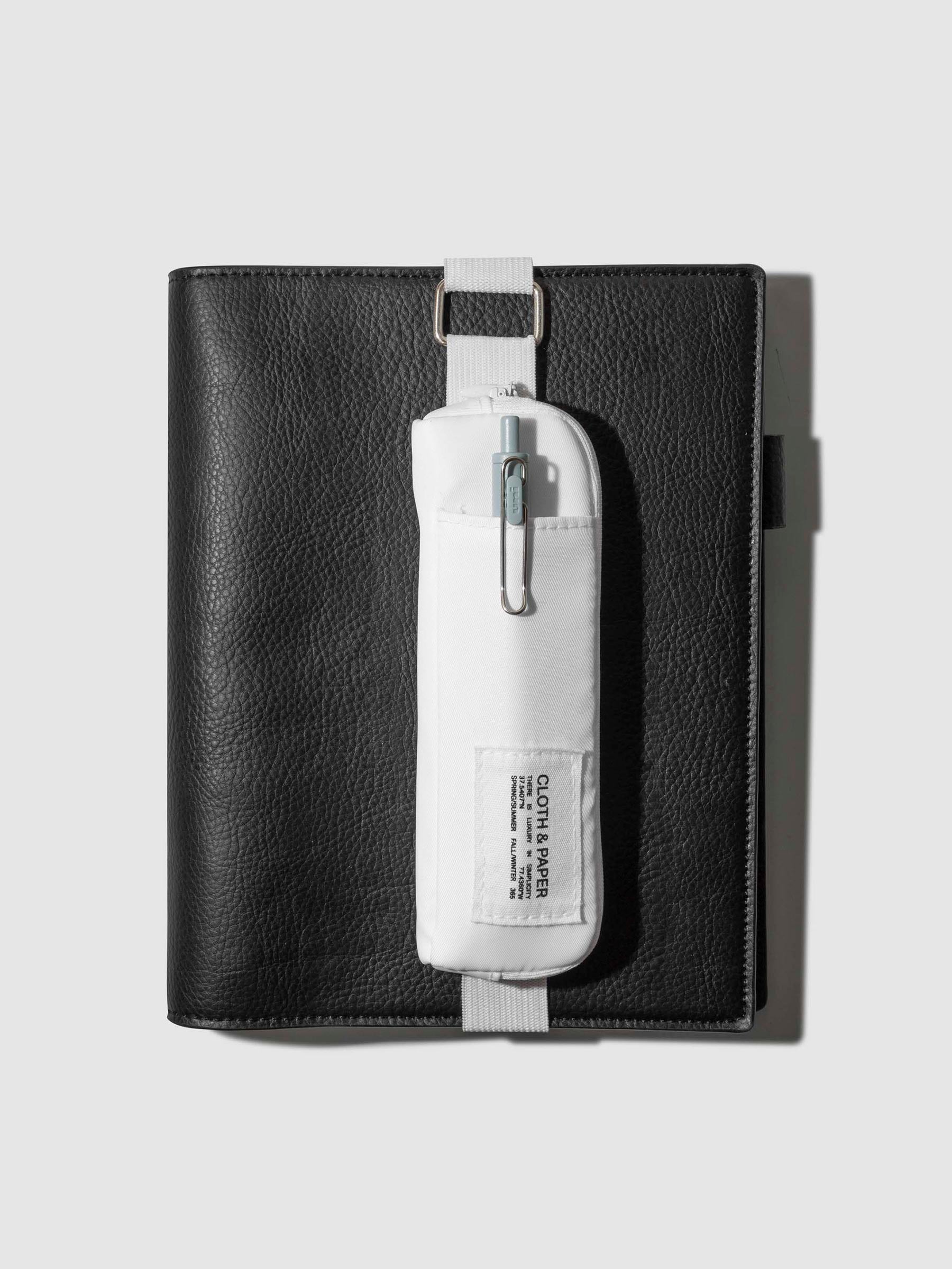 Notebook pouch displayed strapped to a black leather folio on a neutral background. Color shown is Le Blanc.
