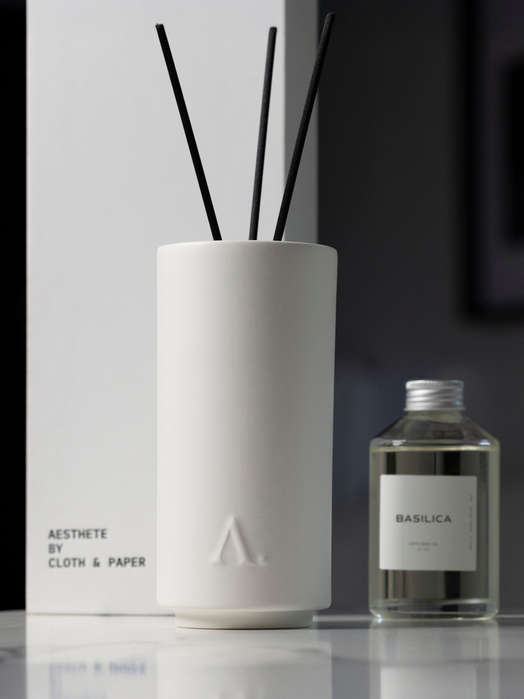 Basilica Diffuser displayed on a table with its packaging and diffuser oil behind it, slightly out of focus.