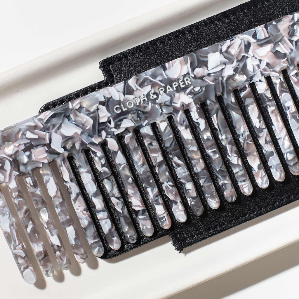 Angled view of the comb, layered on top of the black leather case with a detailed view of Cloth and Paper engraved in the comb