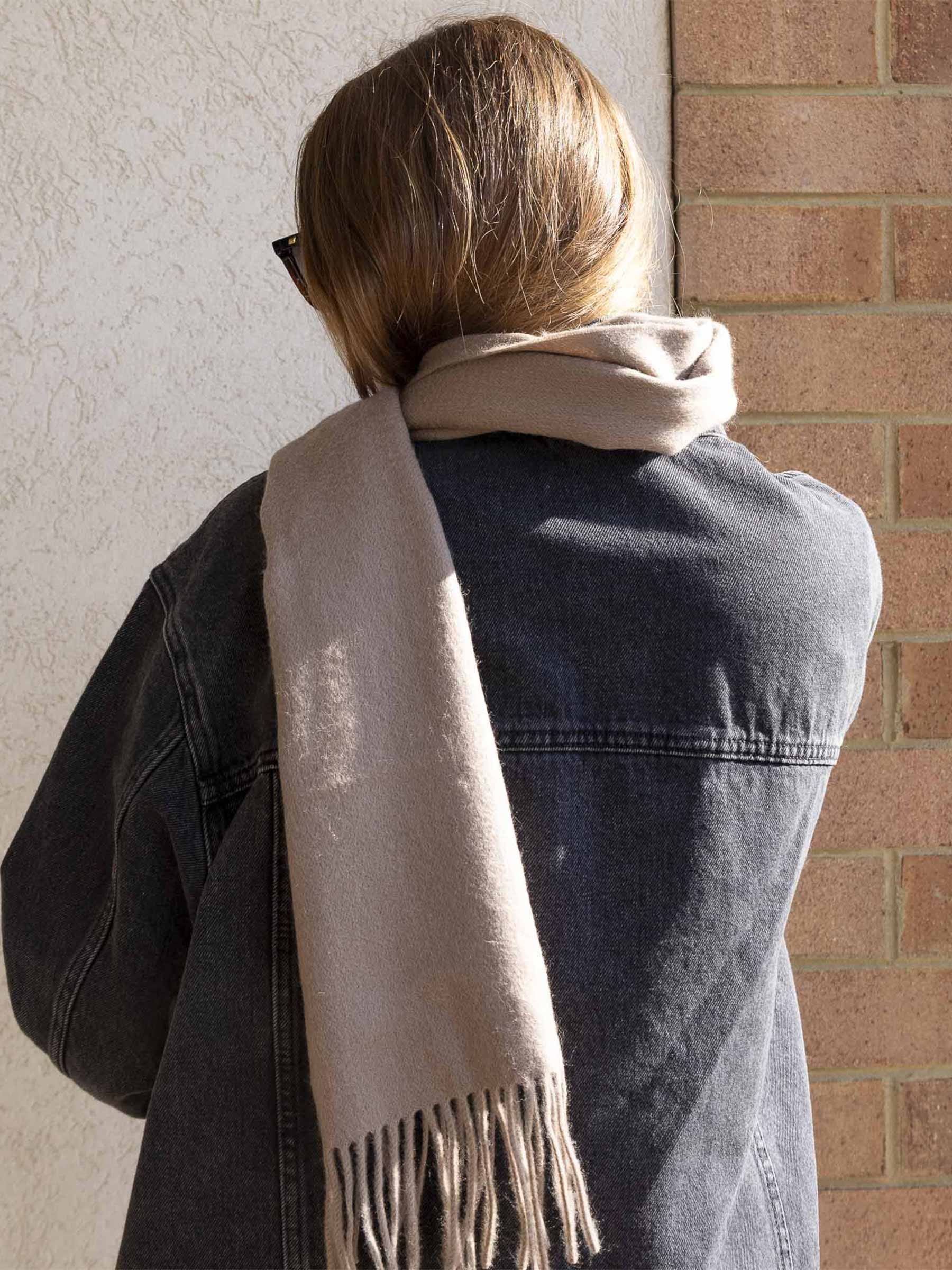 Model shown wearing the Merino wool scarf. She has brown hair, a black jacket, and is lit from the side.