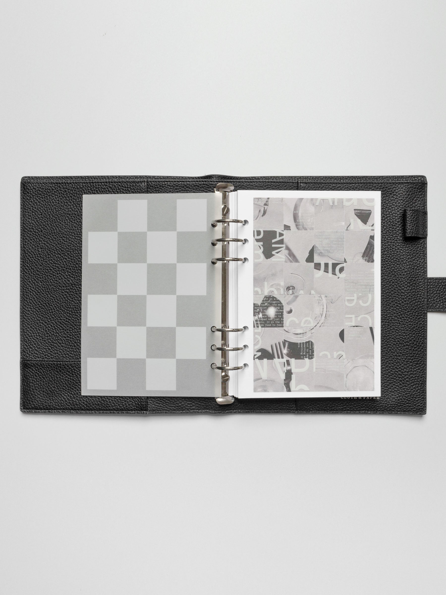 A top-down view of an open planner showing the Ambiance Planner Dashboard trio stacked together. The checkered dashboard is visible on the left, overlaying an abstract design on the right.