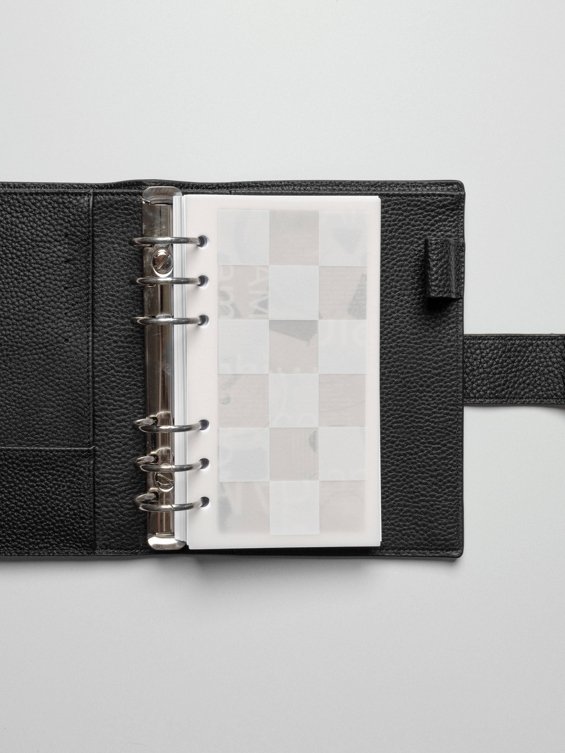 Ambiance Dashboard Trio layered inside a Personal sized black leather planner with silver rings, showcasing the translucent grid layer on top.