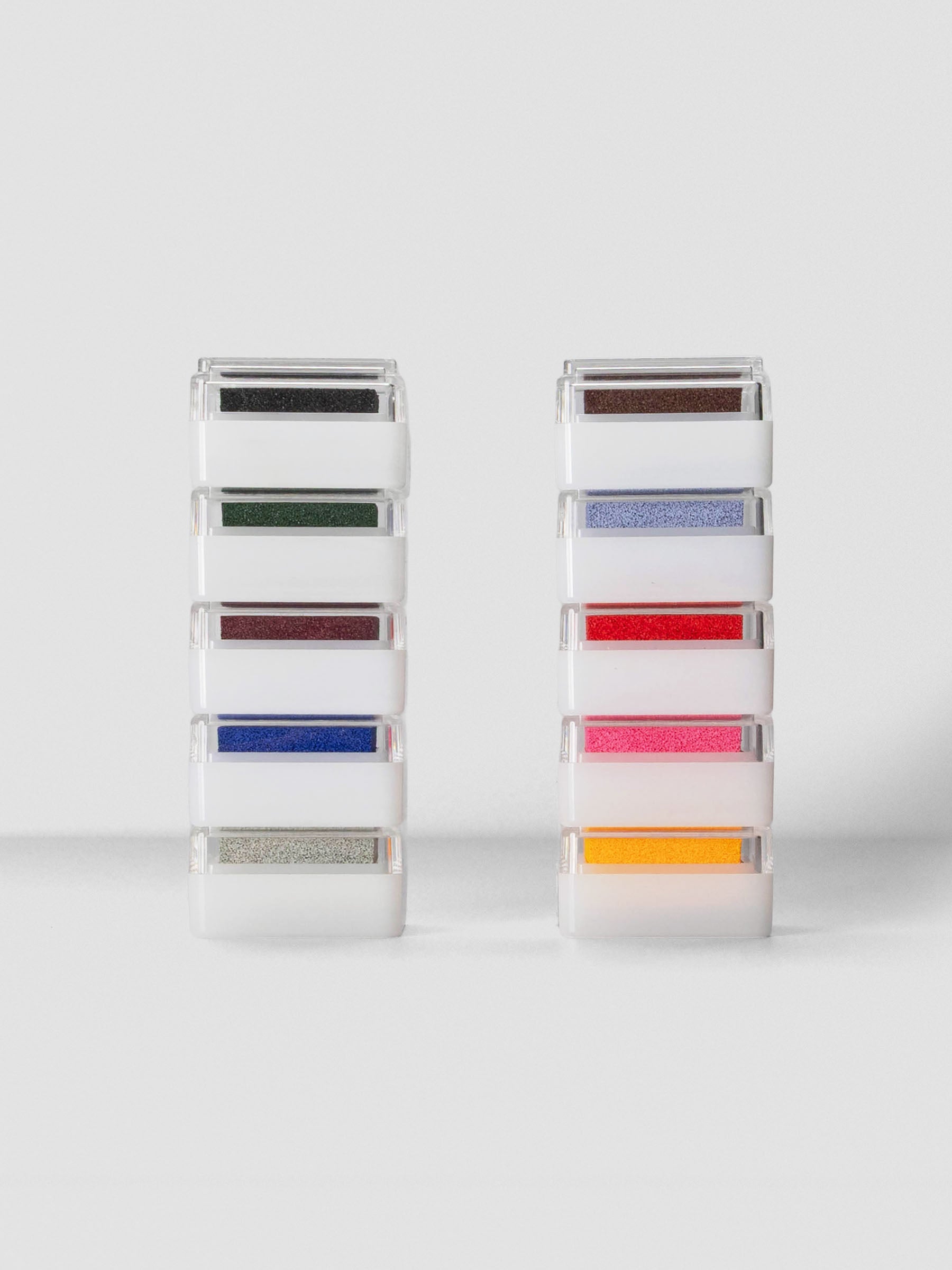 Two vertical stacks of Artnic Stamp Ink Pads in assorted colors with clear lids, arranged on a light gray surface.