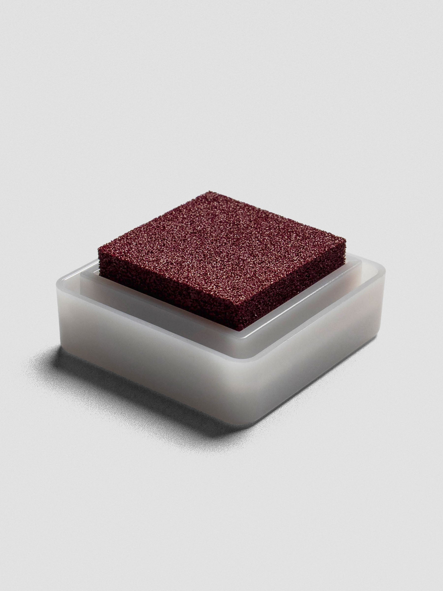 Burgundy Artnic ink pad without lid, angled view of textured ink surface and white base.