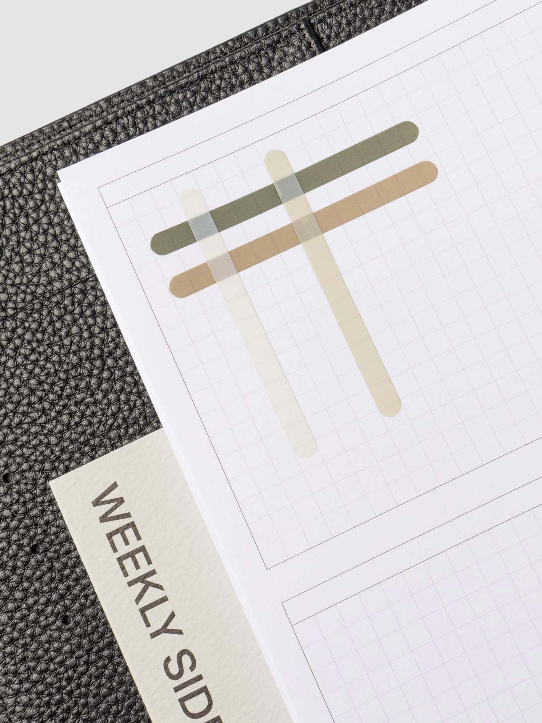 Set of four sticker sheets layered over each other on an insert inside a black leather planner. 