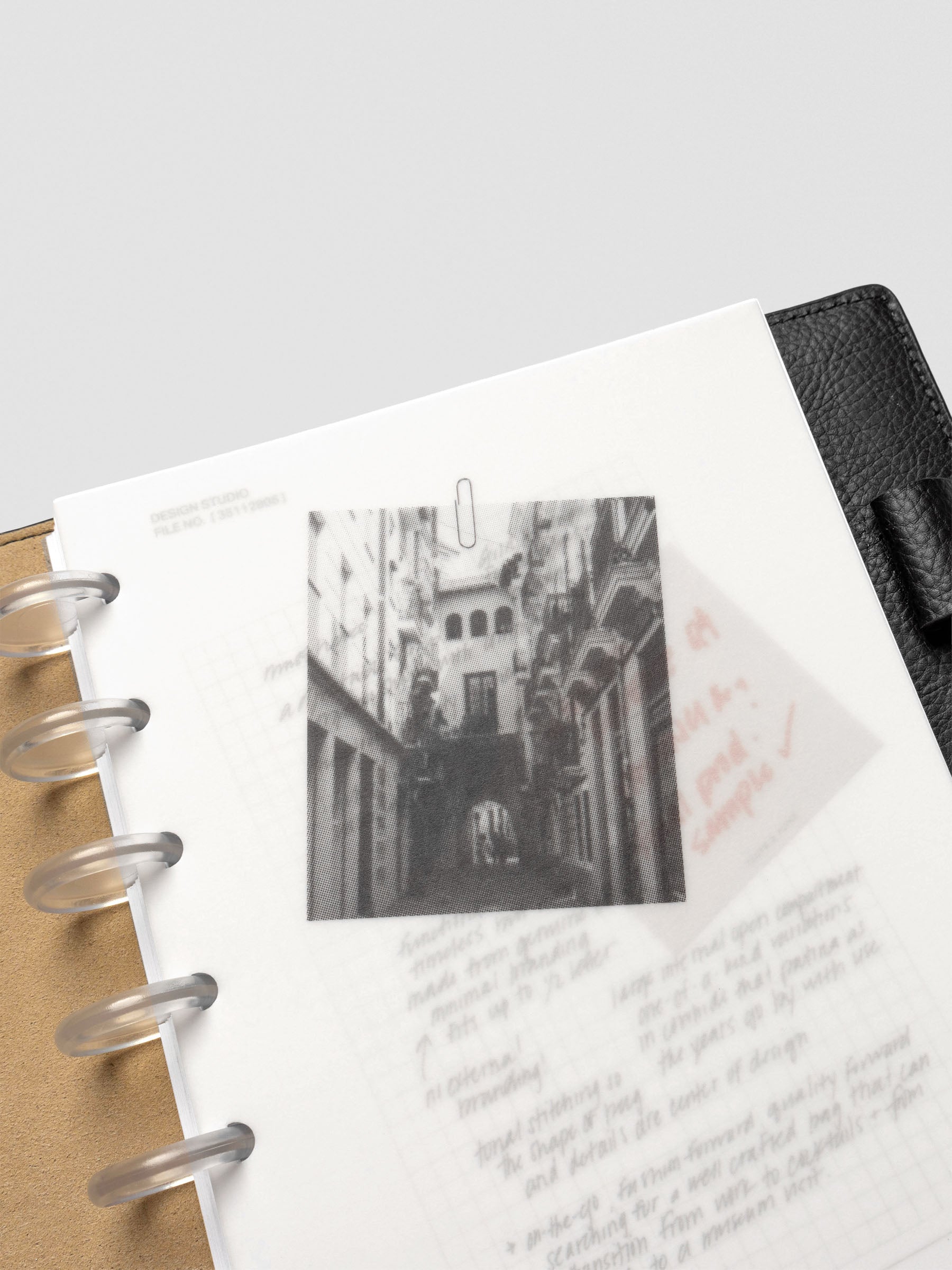 Close-up of a half-letter Behind the Scenes Dashboard Duo insert in a black leather planner. The vellum overlay displays a photograph of an architectural street view over handwritten notes.