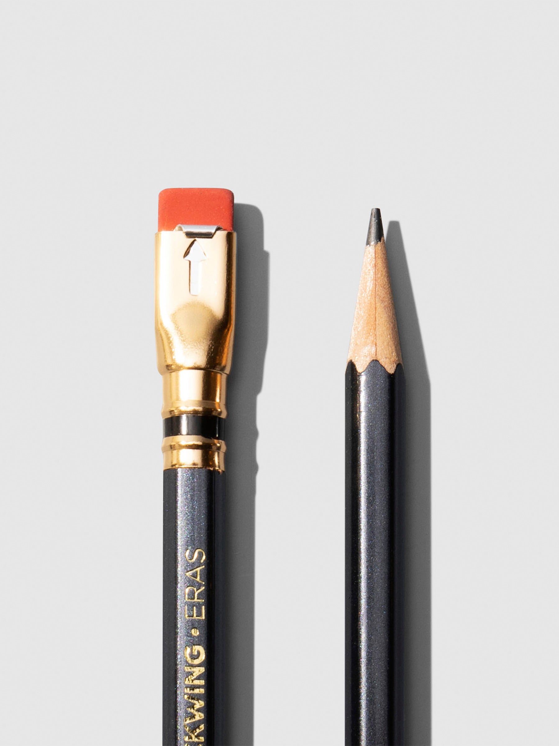 Closeup of two black wooden pencils displayed on a neutral background. One is shown eraser side up, the other point side up.
