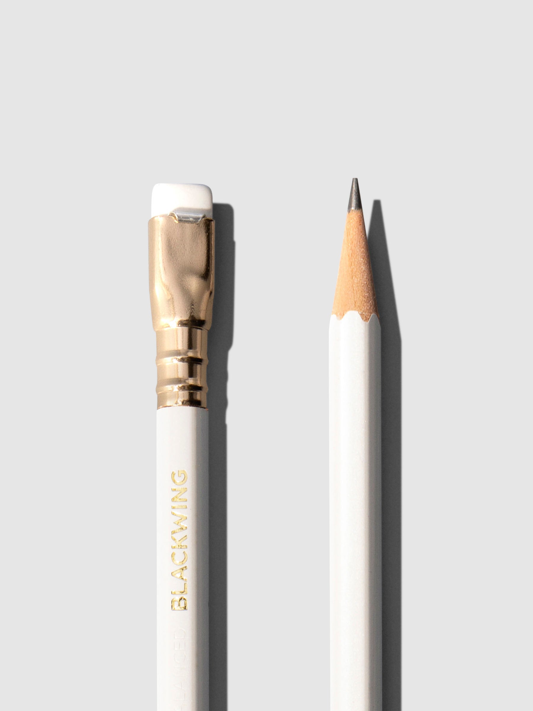 Closeup of two white wooden pencils displayed on a neutral background. One is shown eraser side up, the other point side up.