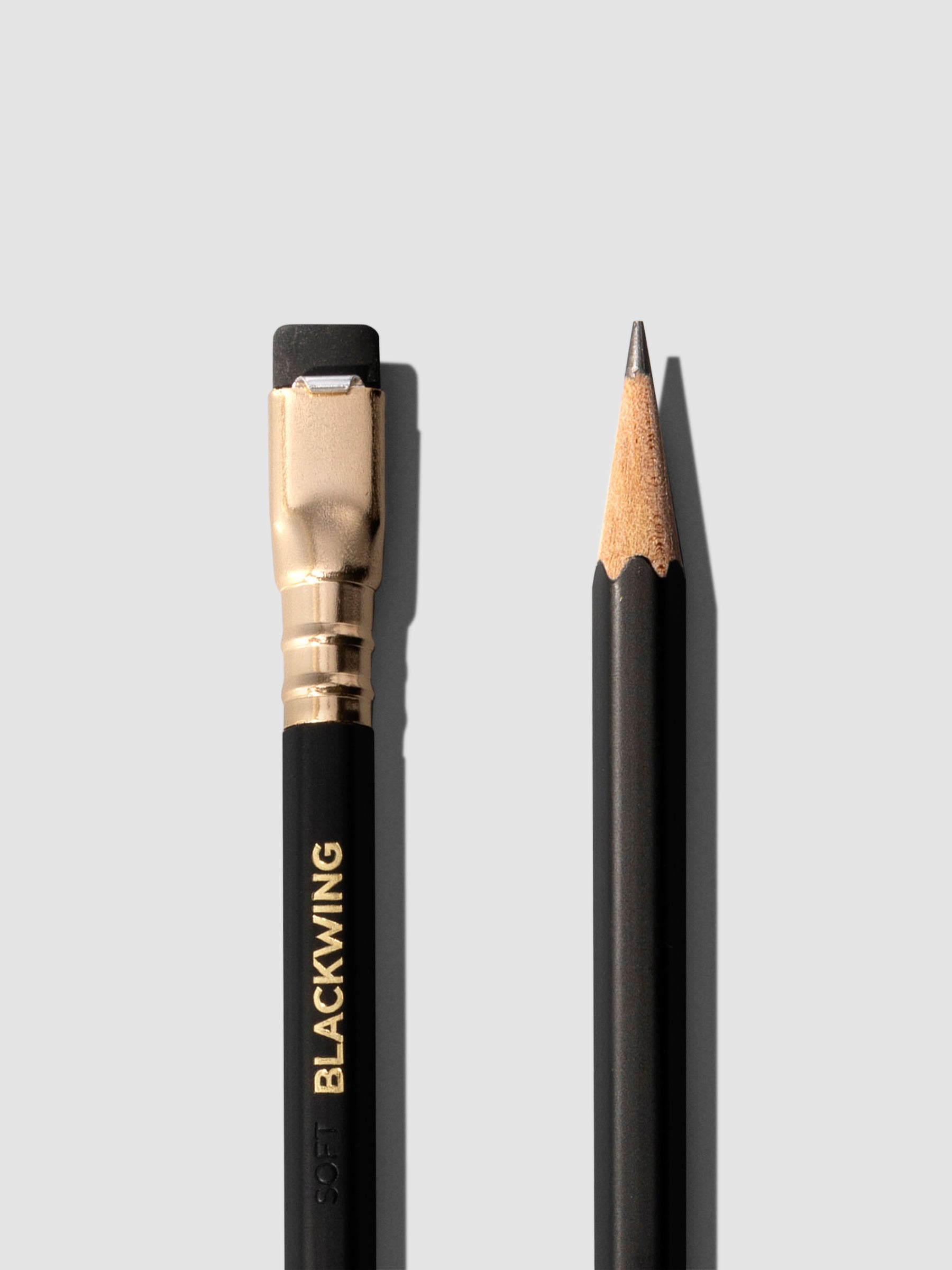Closeup of two black wooden pencils displayed on a neutral background. One is shown eraser side up, the other point side up.