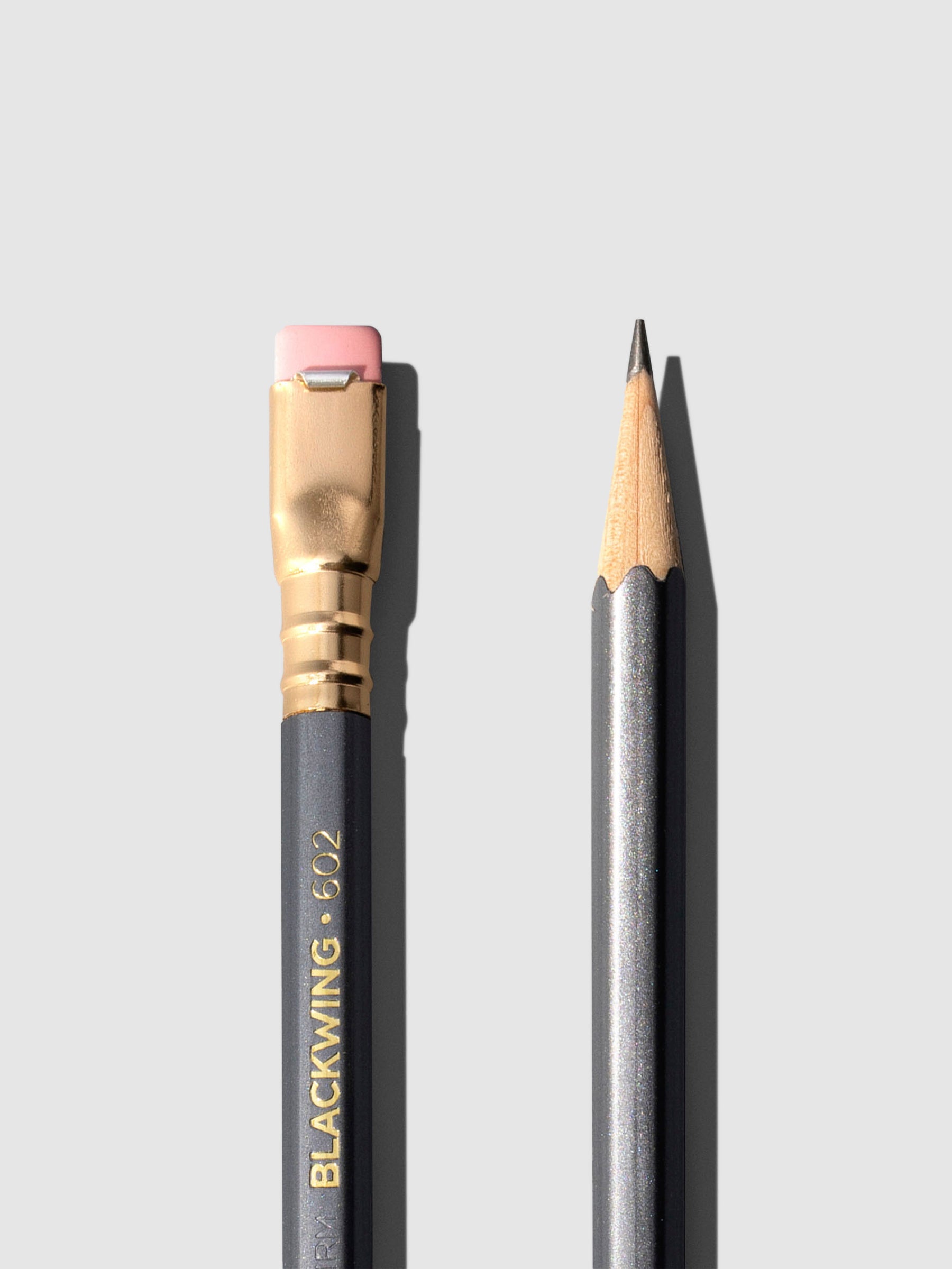 Closeup of two gray wooden pencils displayed on a neutral background. One is shown eraser side up, the other point side up.