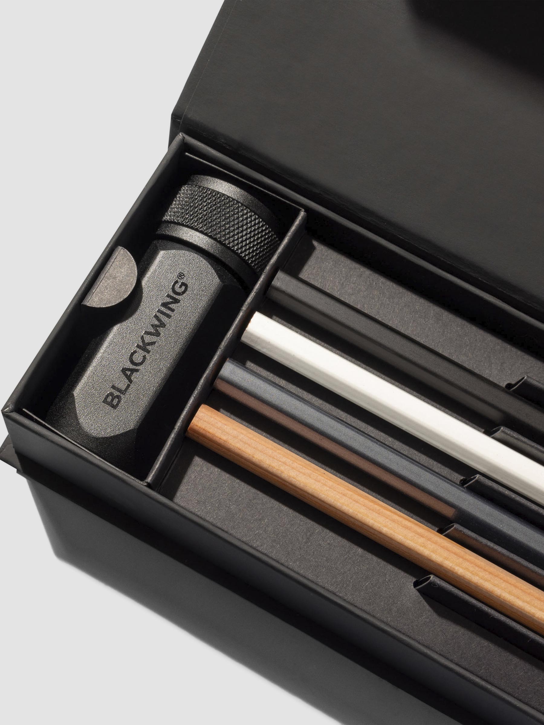 Closeup of four pencils and black pencil sharpener inside black storage box.