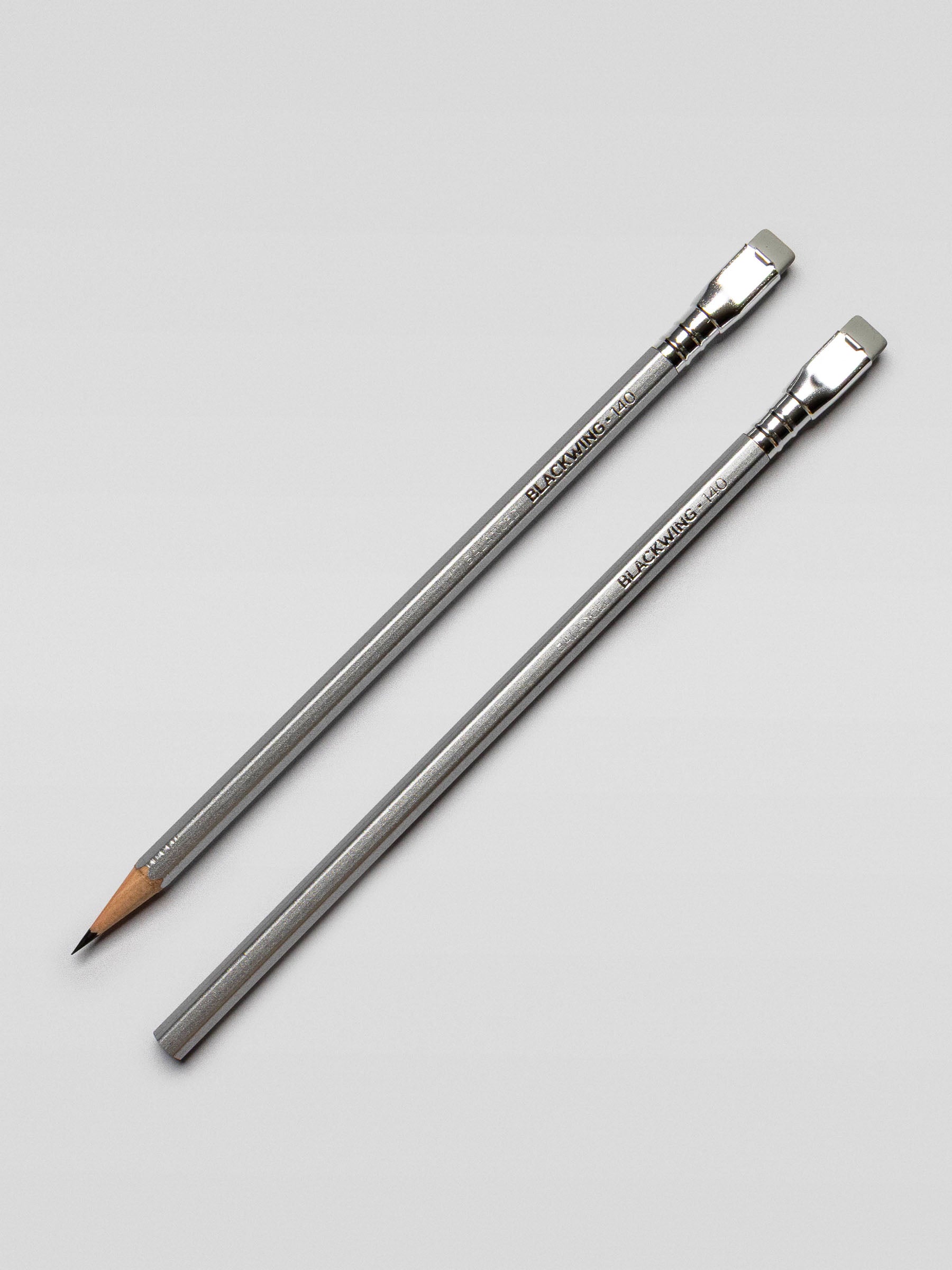 Two Blackwing 140 pencils laid side by side on a light surface, one sharpened and one unsharpened, highlighting the metallic finish.