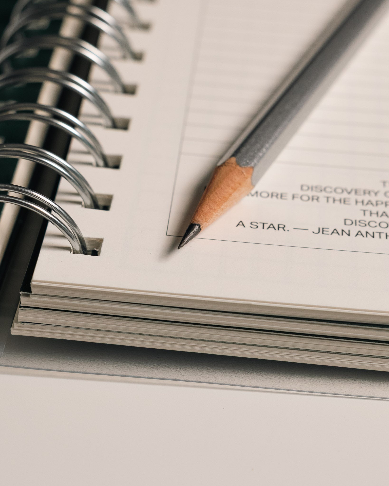 Close-up of the sharpened tip of a Blackwing 140 pencil resting on a planner page with spiral binding.