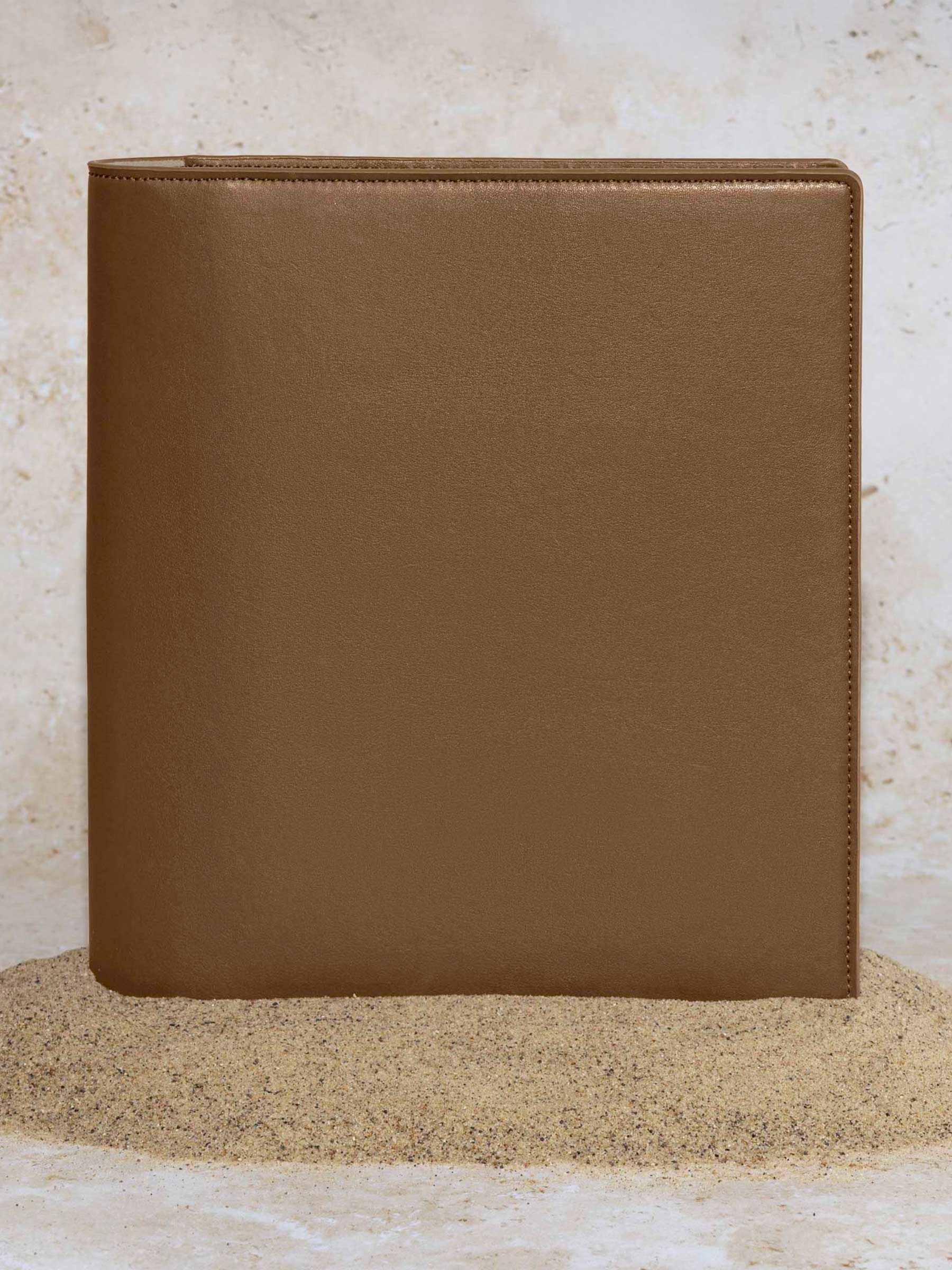Folio displayed on a textured tan background, placed in a pile of sand. Color pictured is clay brown. 