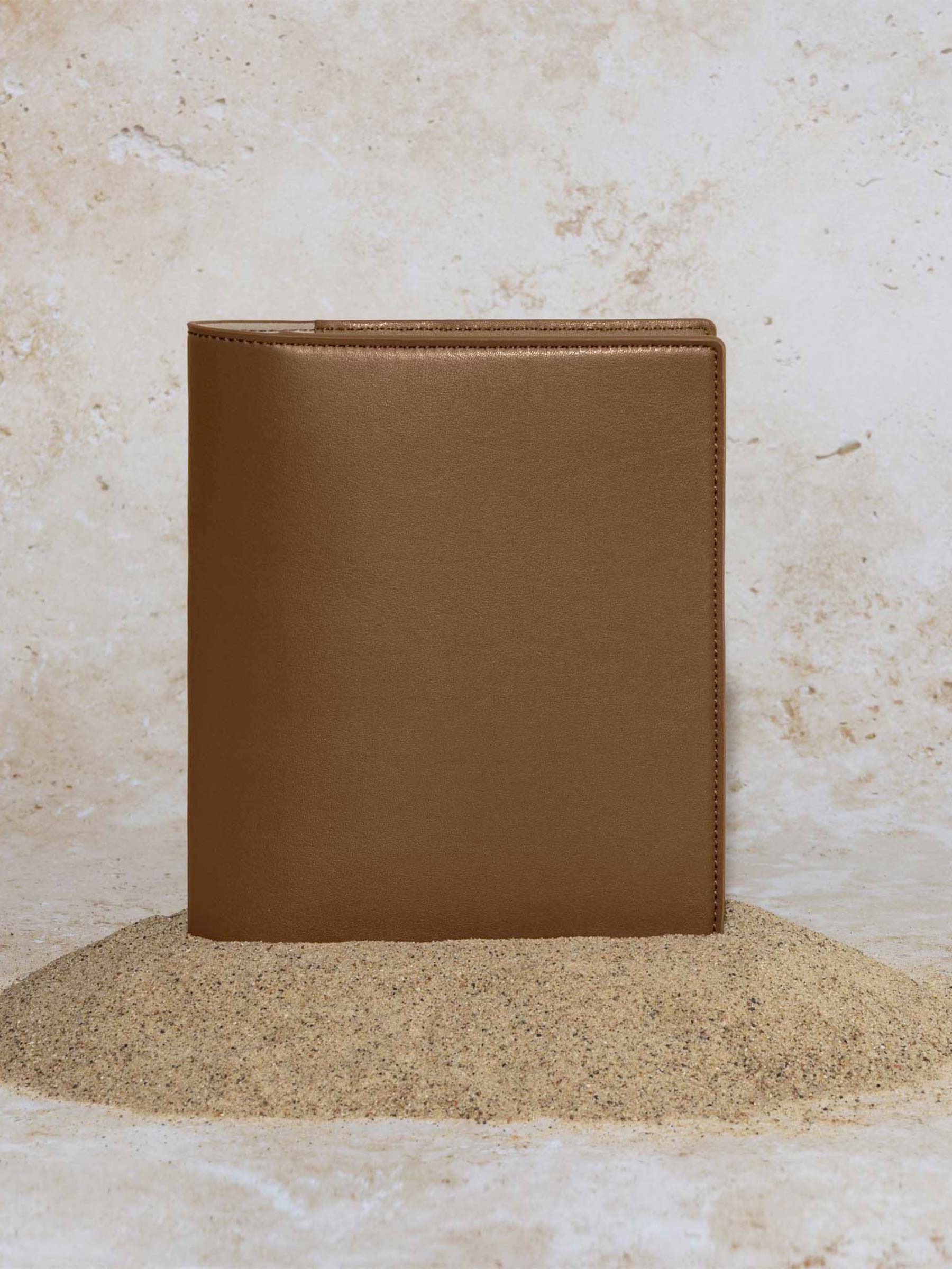 Folio displayed on a textured tan background, placed in a pile of sand. Color pictured is clay brown.