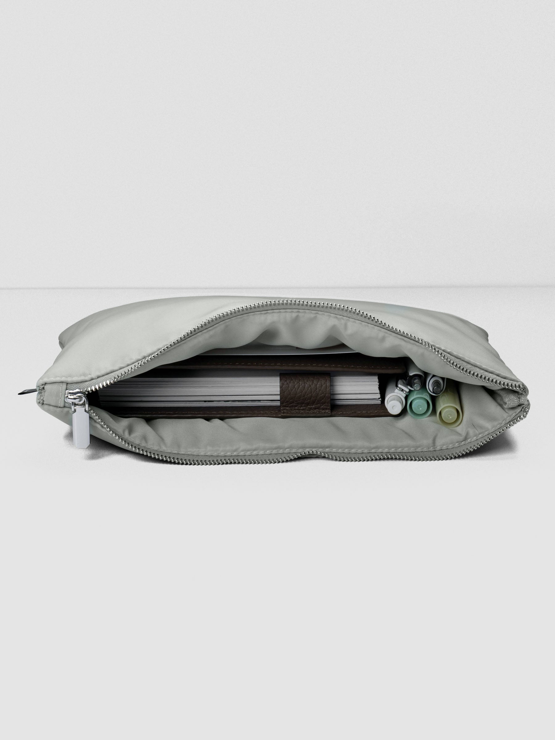 Light green-grey nylon, zippered, padded travel case shown laying down, open with a planner and writing accessories inside.