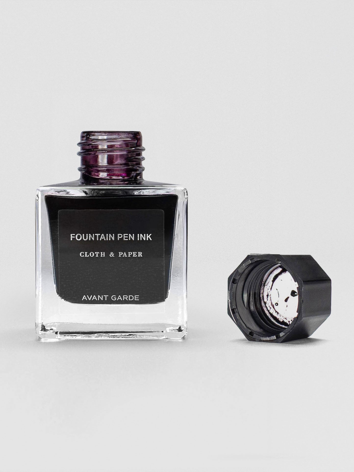 The Avant Garde ink bottle shown open, with the black cap set beside it, revealing a deep ink inside.