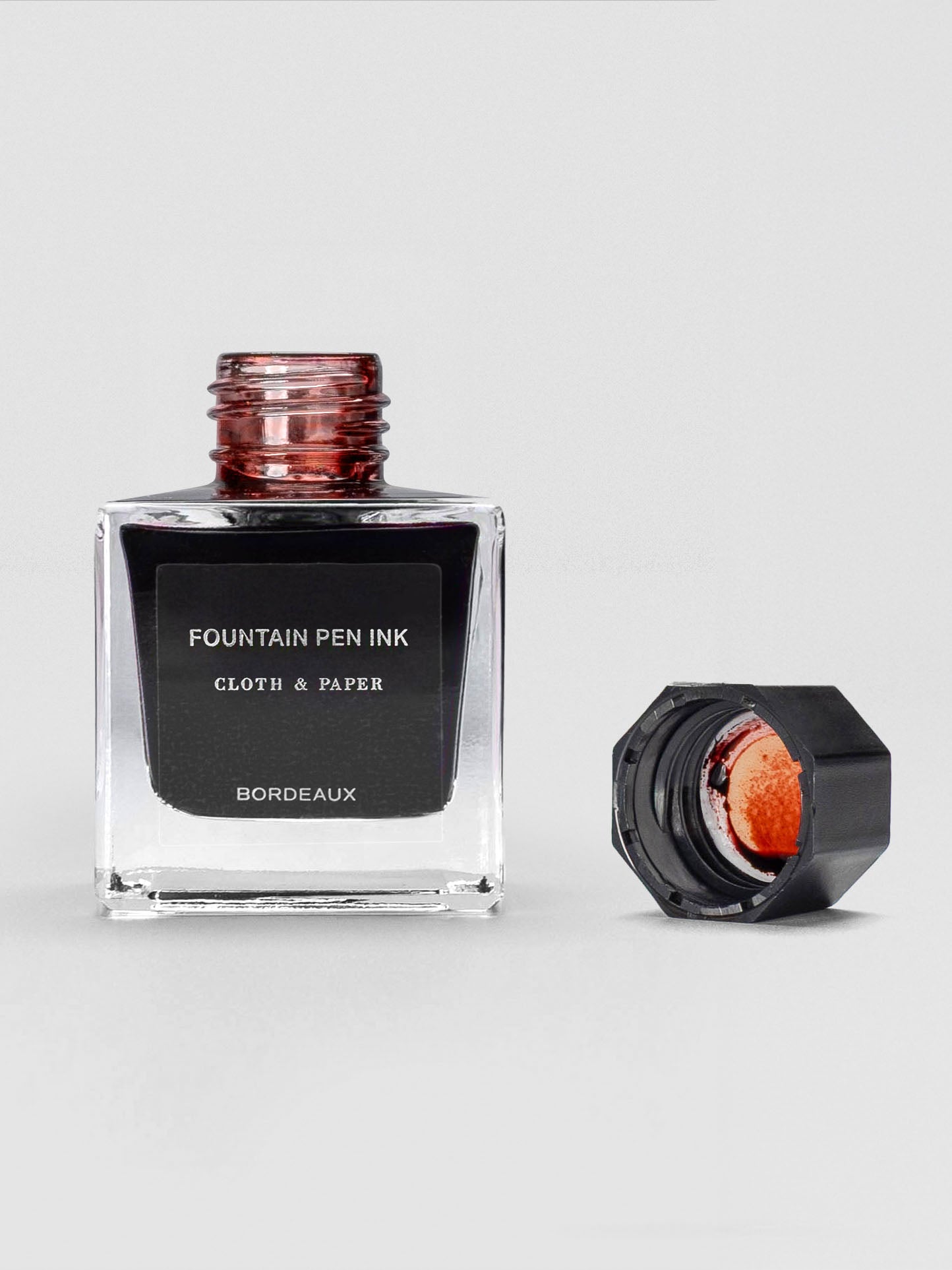 The Bordeaux ink bottle shown open, with the black cap set beside it, revealing rich red ink inside.
