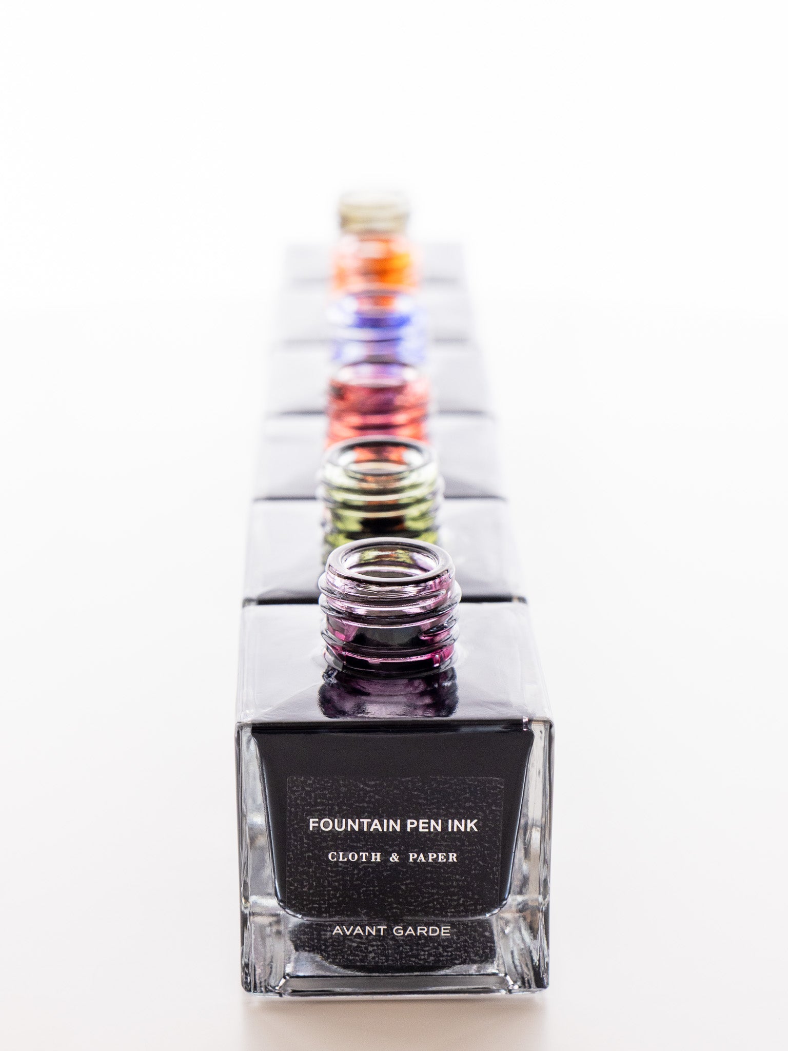 Row of open Cloth & Paper fountain pen ink bottles photographed from above, with Avant Garde in front and colorful ink residues visible on rims.