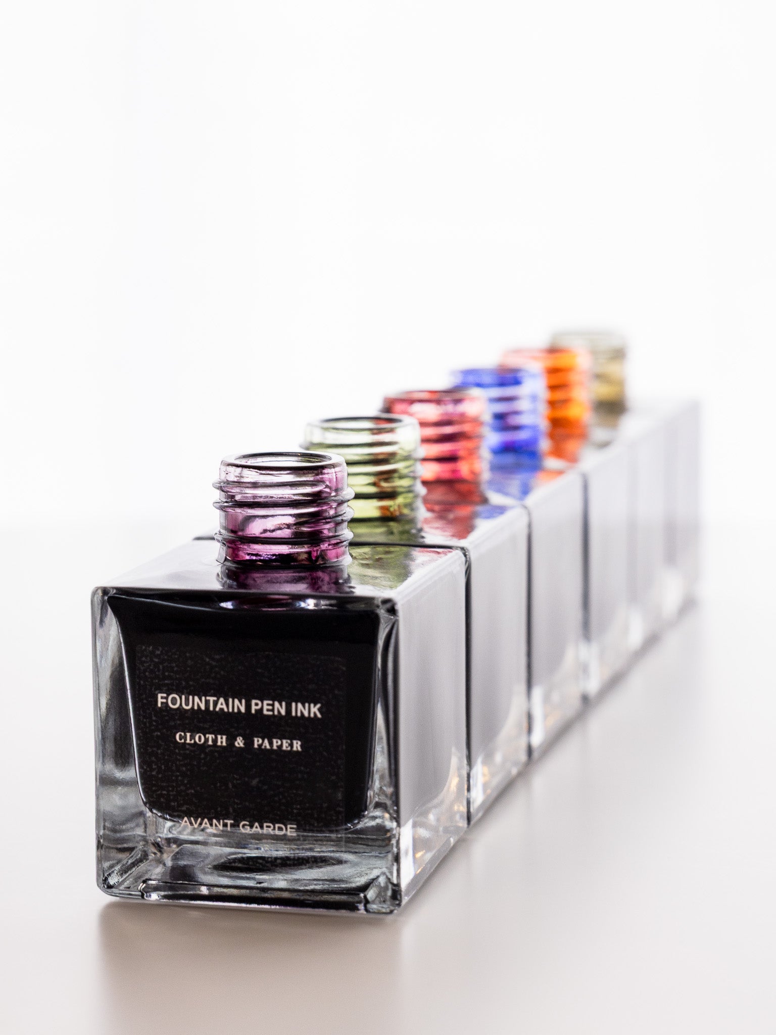 Diagonal view of multiple Cloth & Paper fountain pen ink bottles lined up, with Avant Garde in front and ink colors visible across the bottle tops.