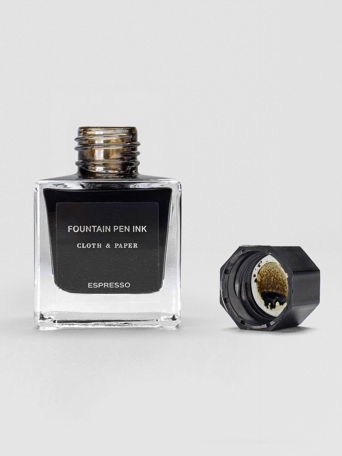 The Espresso ink bottle shown open, with the black cap set beside it, revealing dark brown ink inside.