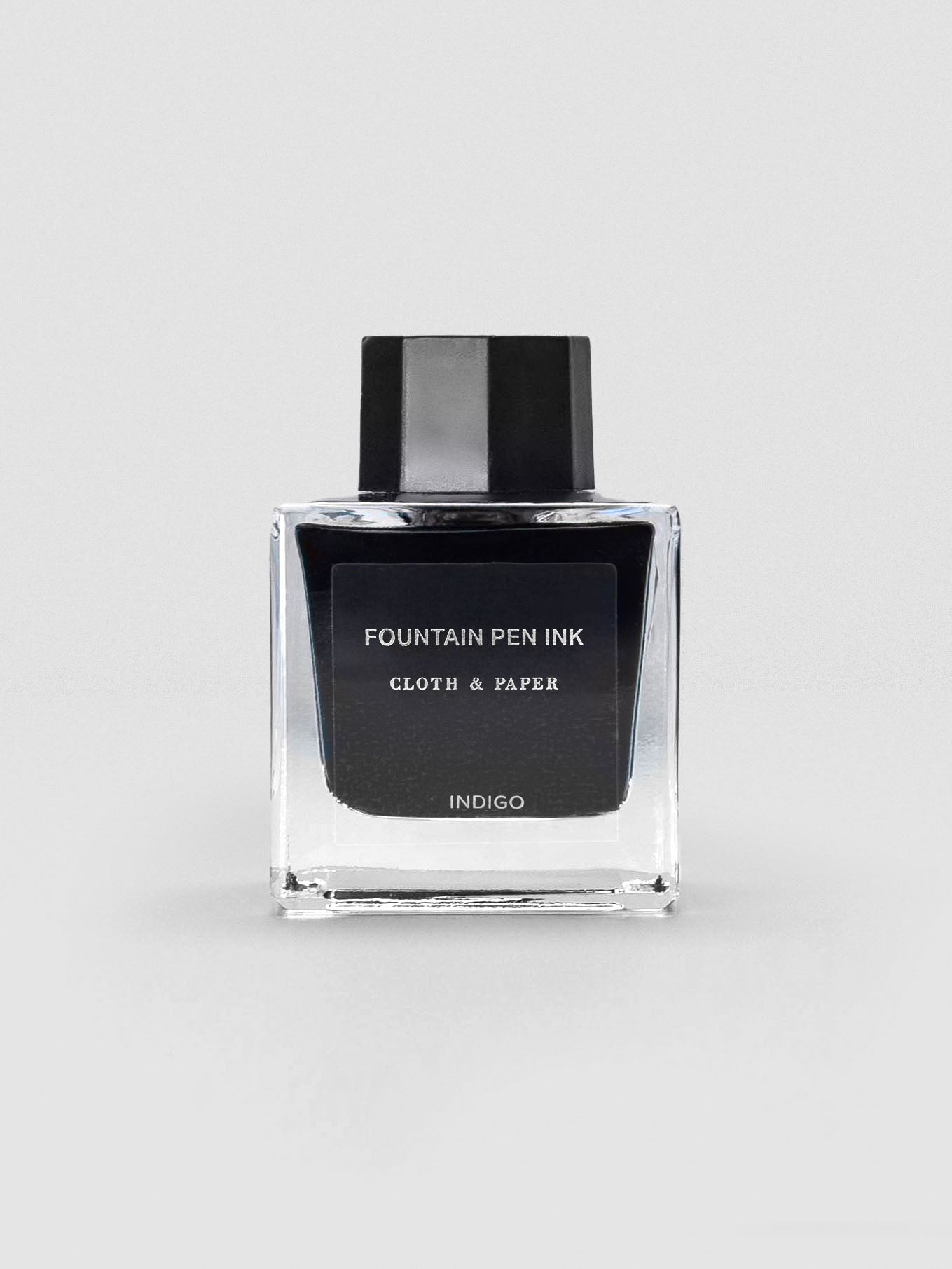 A square glass bottle of Cloth & Paper Fountain Pen Ink in Indigo, shown with a black label and matching black cap.