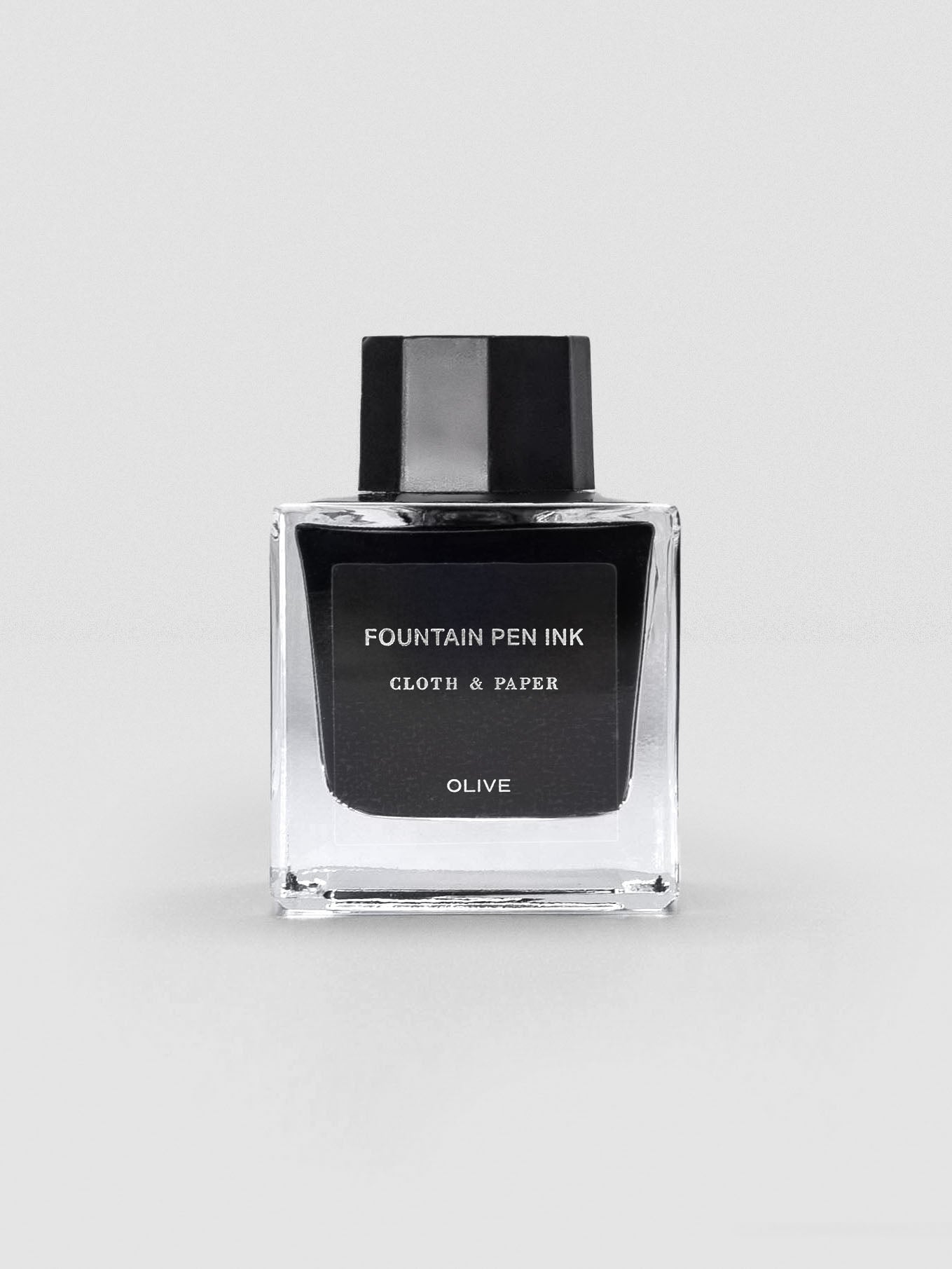 A square glass bottle of Cloth & Paper Fountain Pen Ink in Olive, displayed with a sleek black label and black cap.