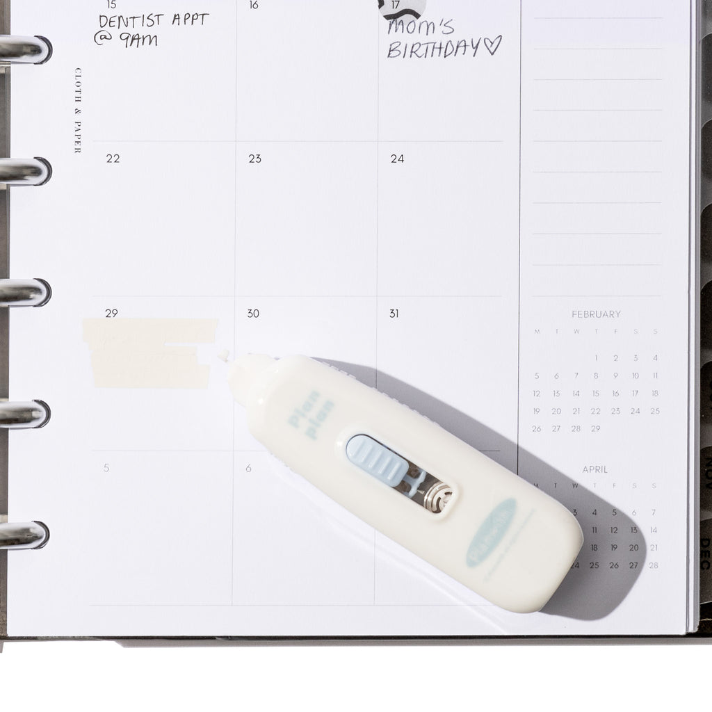 White pen displayed resting on a calendar insert. One calendar square is shown with correction tape used on it.