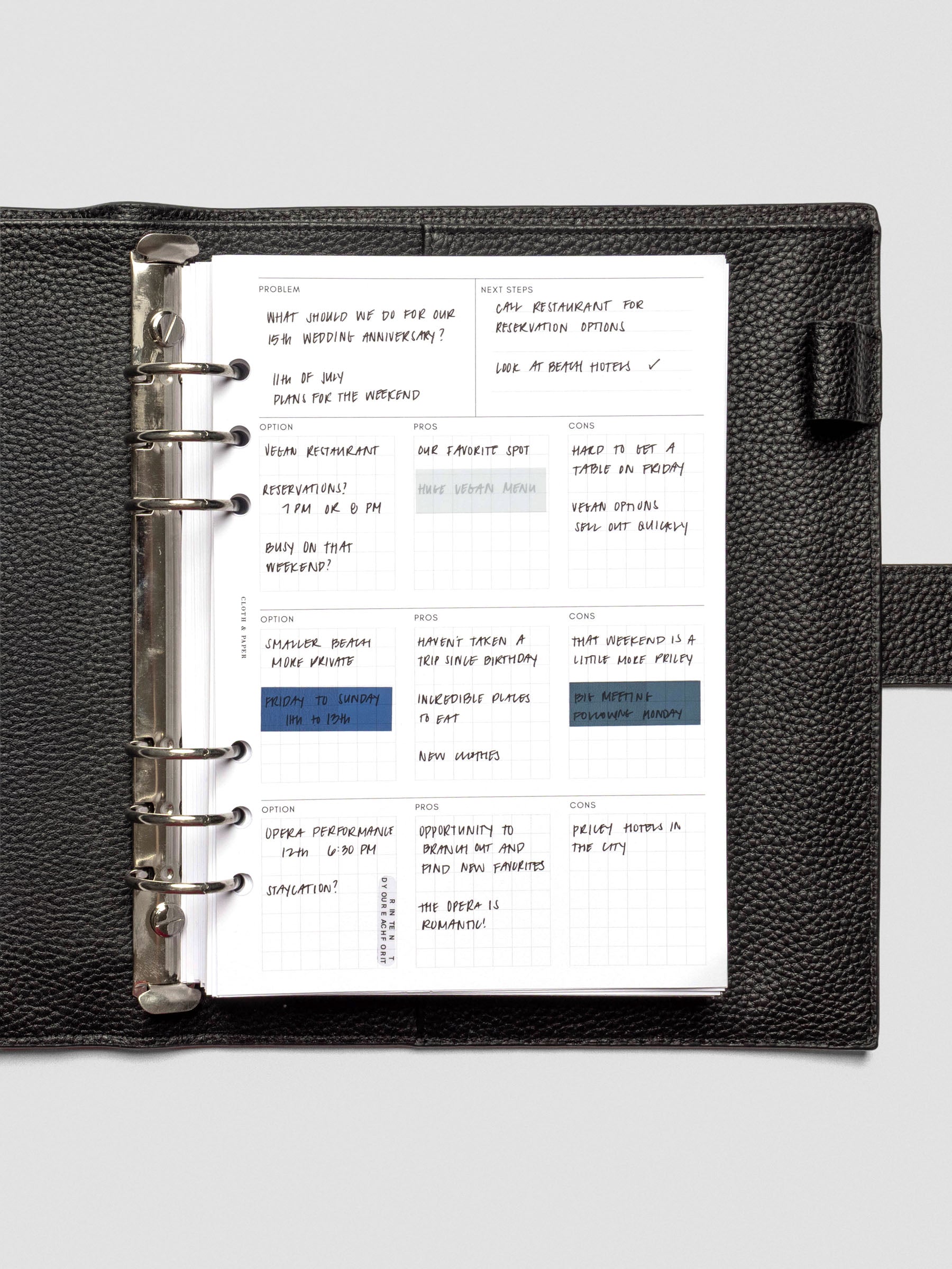 An A5 decision-making insert inside a black leather six-ring planner, completed with handwritten notes across problem, next steps, and option grids with pros and cons.
