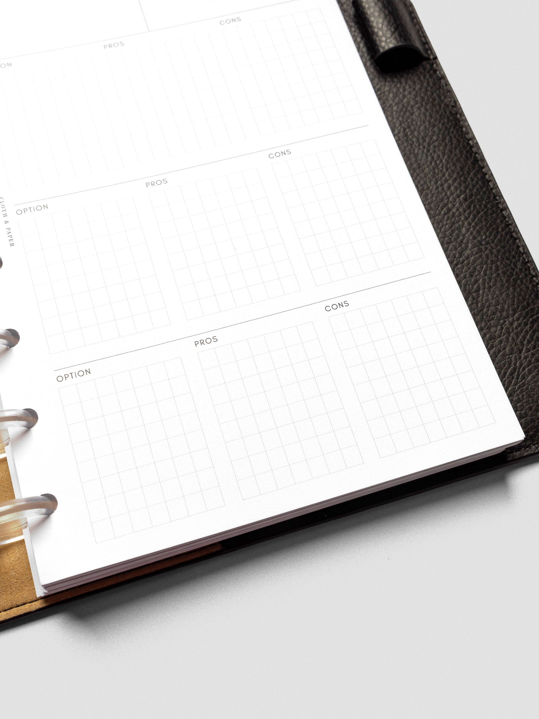 Detail view of a half-letter decision-making insert inside a black leather planner. The page shows multiple gridded sections labeled option, pros, and cons.