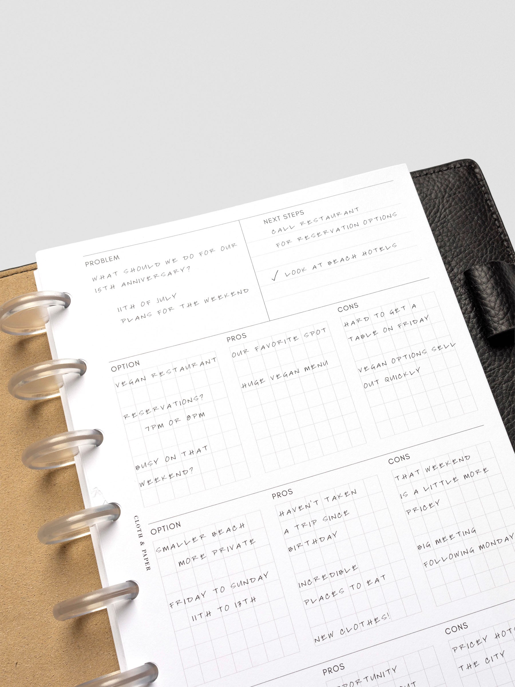 Close-up of a half-letter decision-making insert inside a black leather planner, handwritten with notes on problem, next steps, and option grids for pros and cons.