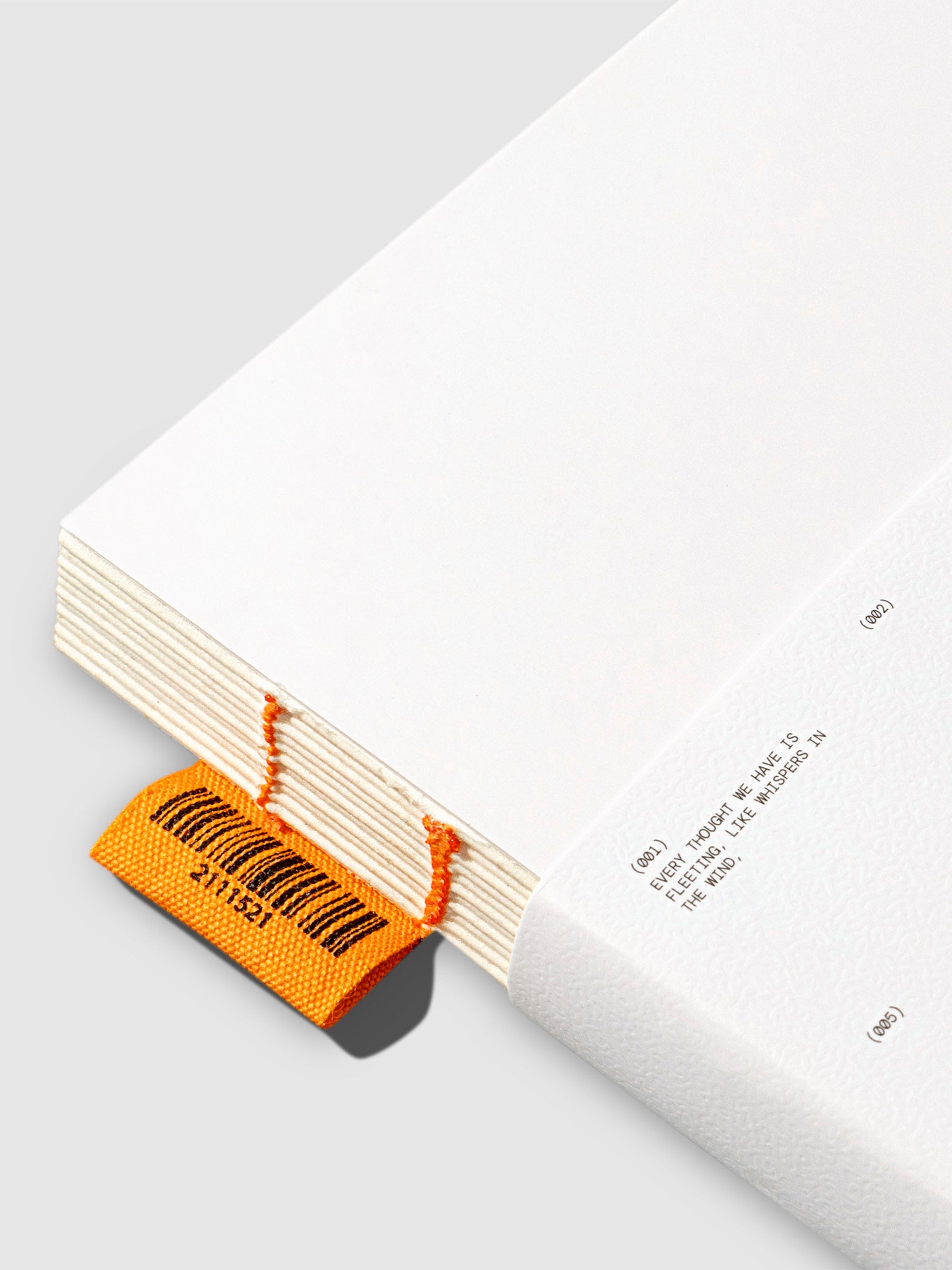 Notebook displayed on a neutral background. Focus is on orange tag sewn into the book.