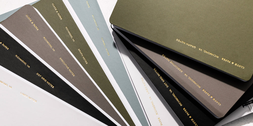 an image representing the different colors and styles available for our España Spiral Notebooks.  In order left to right are Lined in Ash, Dot Grid in Avant Garde, Executive Notes in Cafe Noir, Graph Notes in Olive, and Cornell Notes in Mykonos. 