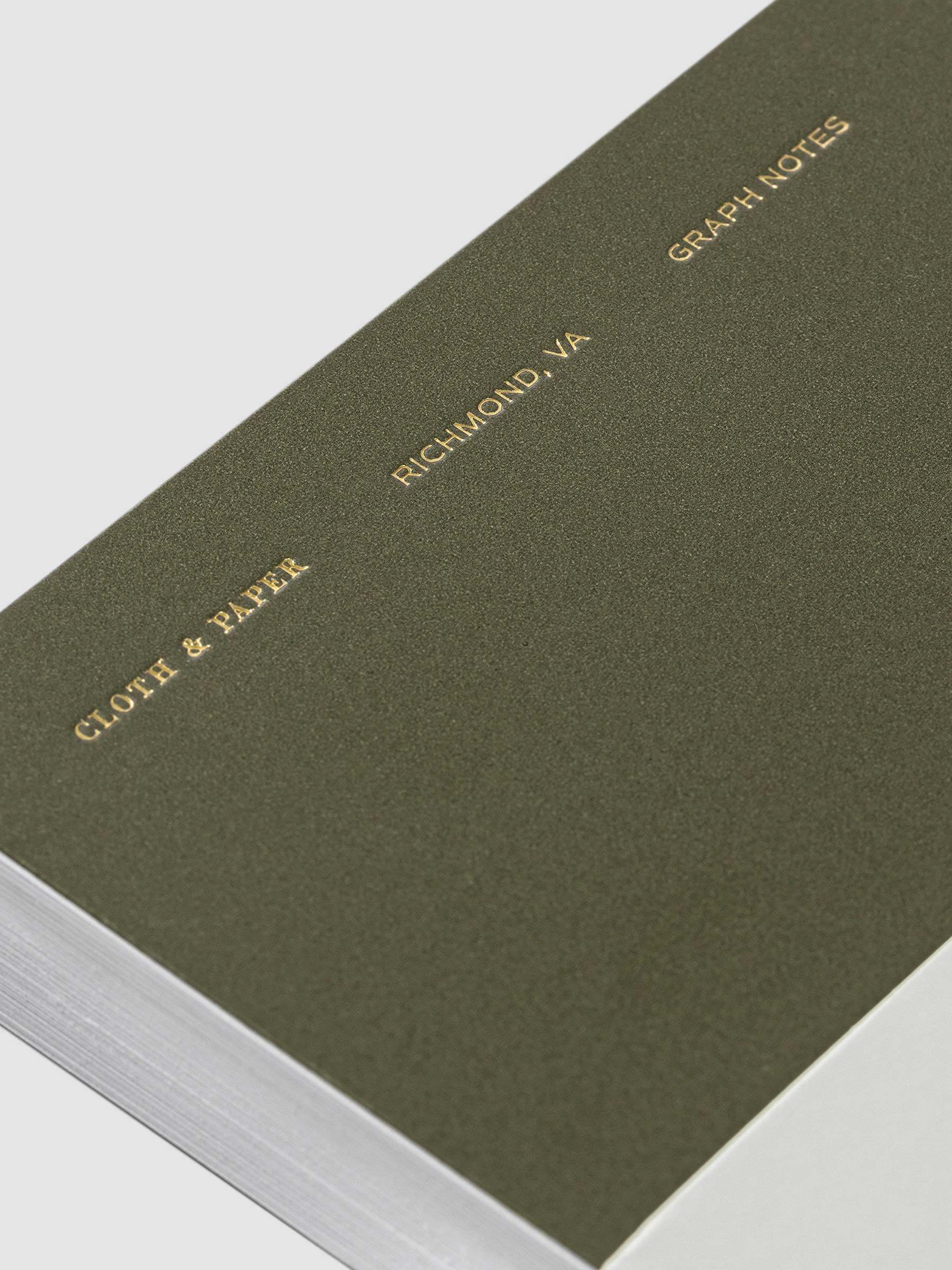Closeup of text on Olive notebook. From bottom to top, it reads "Cloth & Paper / Richmond, VA / Graph Notes"